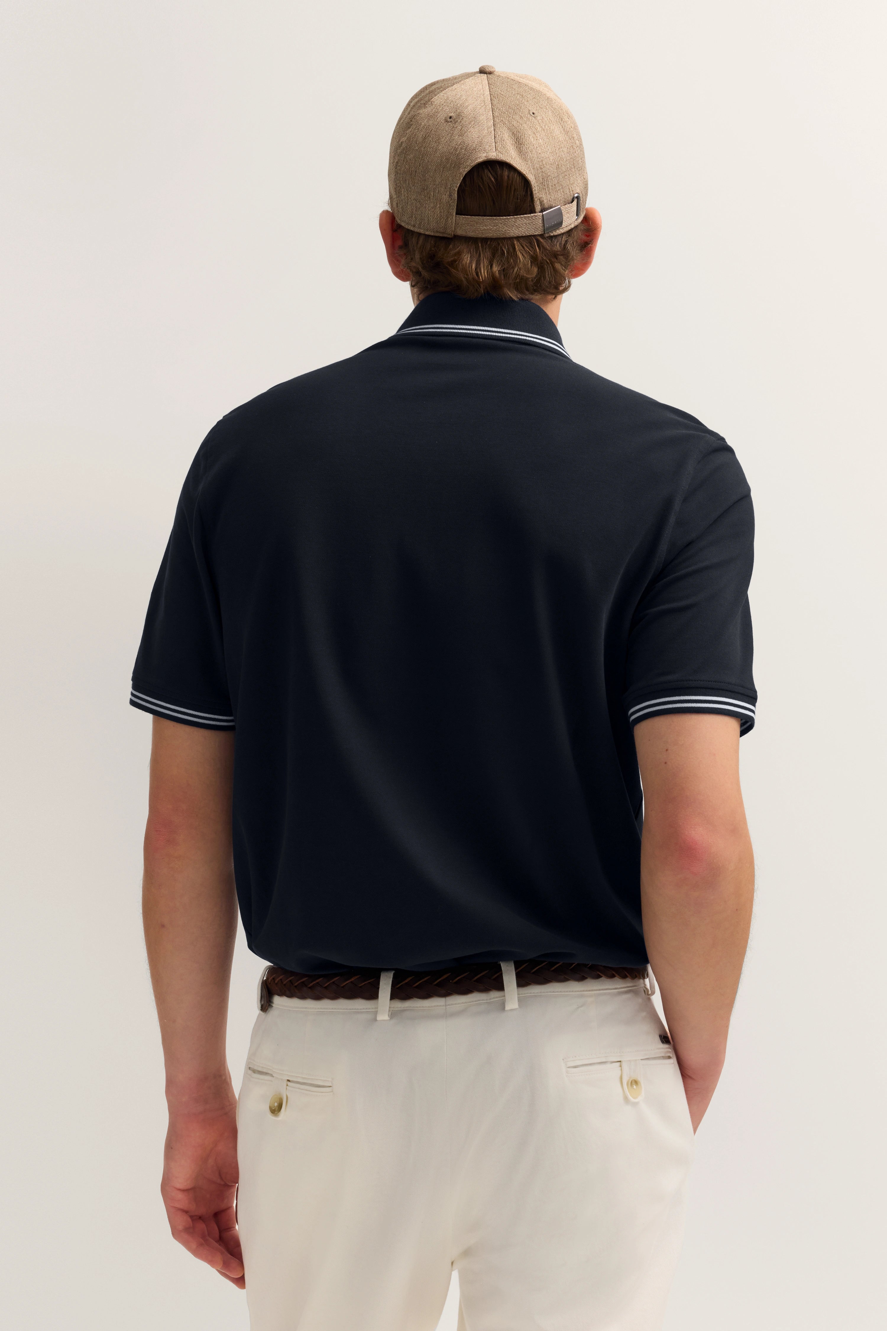 Rückansicht: Navy-Poloshirt, beige Cap, weiße Hose. Leger und stilvoll von bugatti.