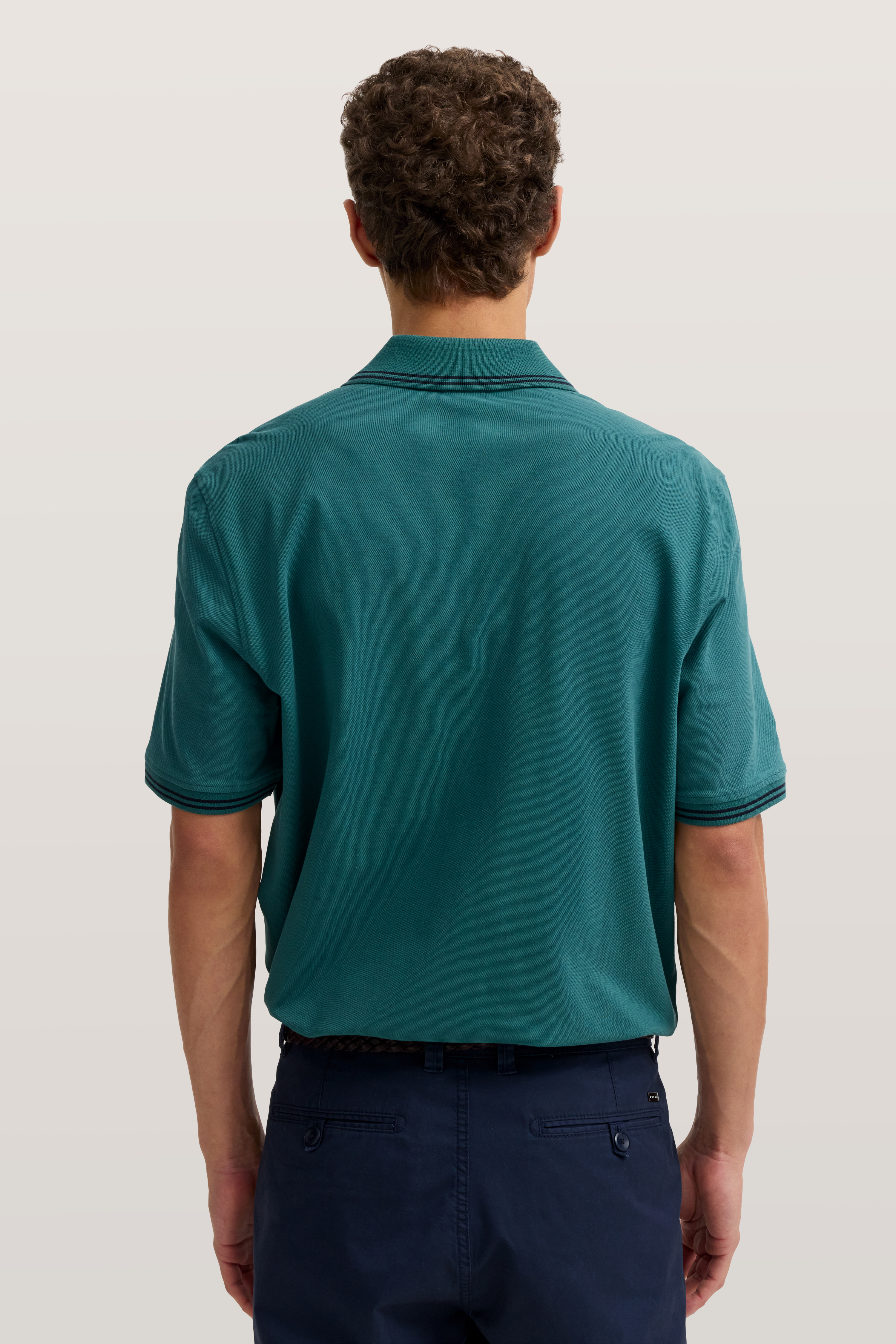 Herrenmodell von hinten in grünem Polo und blauer Hose, legeres Posing.