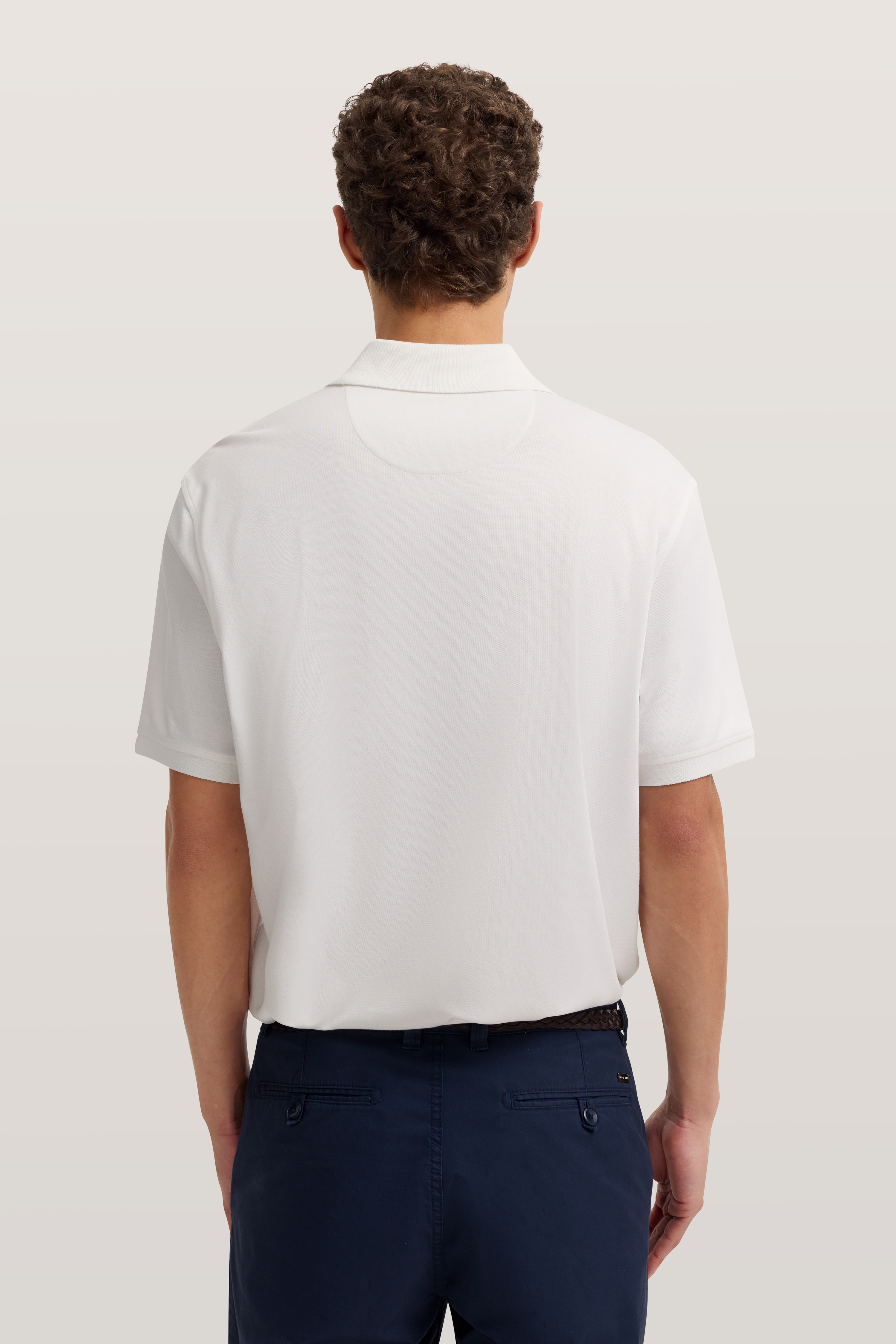 Weißes Polohemd von bugatti, Modellrückansicht, kombiniert mit dunkelblauer Hose.