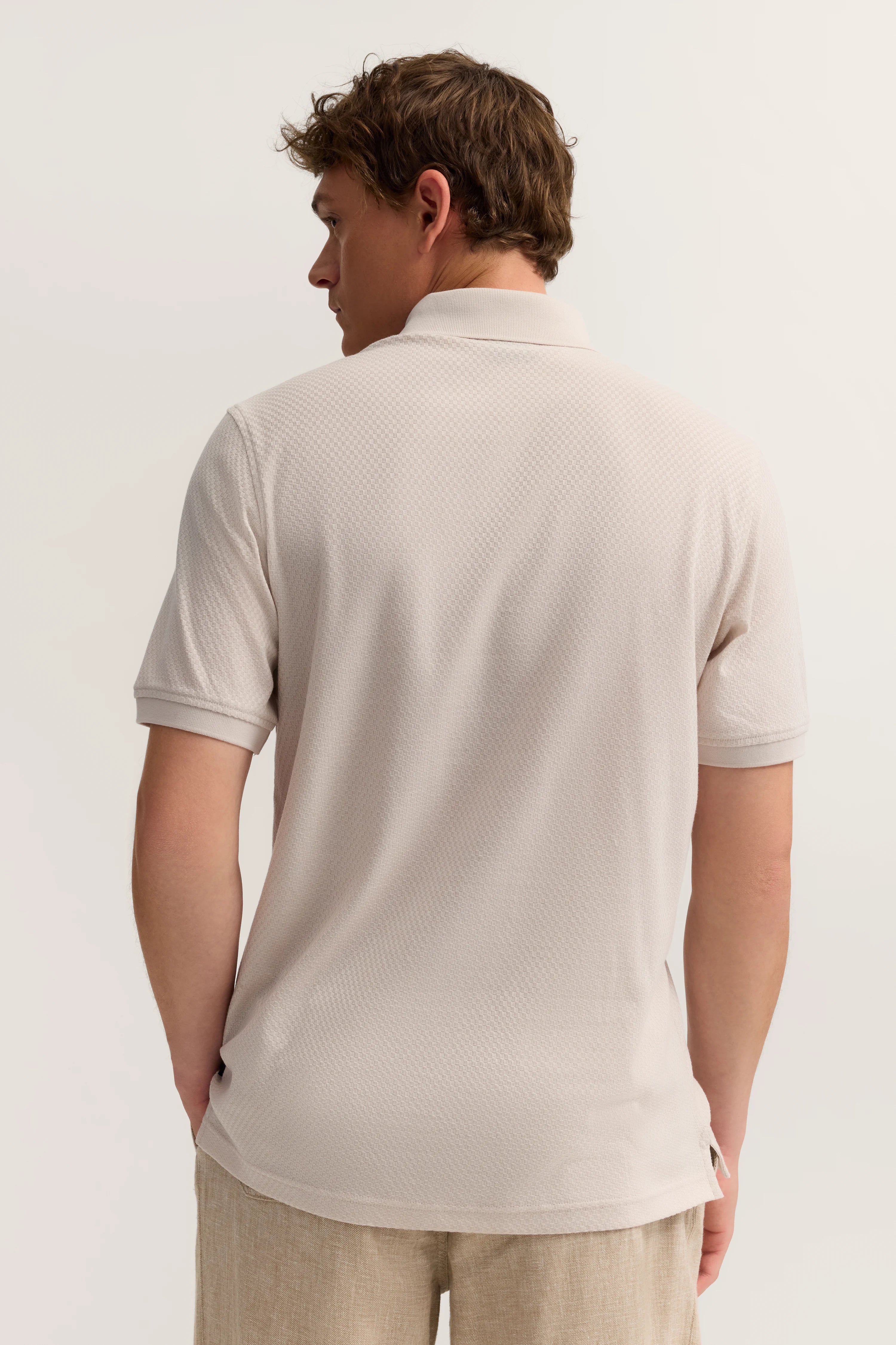 Herrenmodell in beige Polo-Shirt von hinten, beige Hose, relaxed Posing.