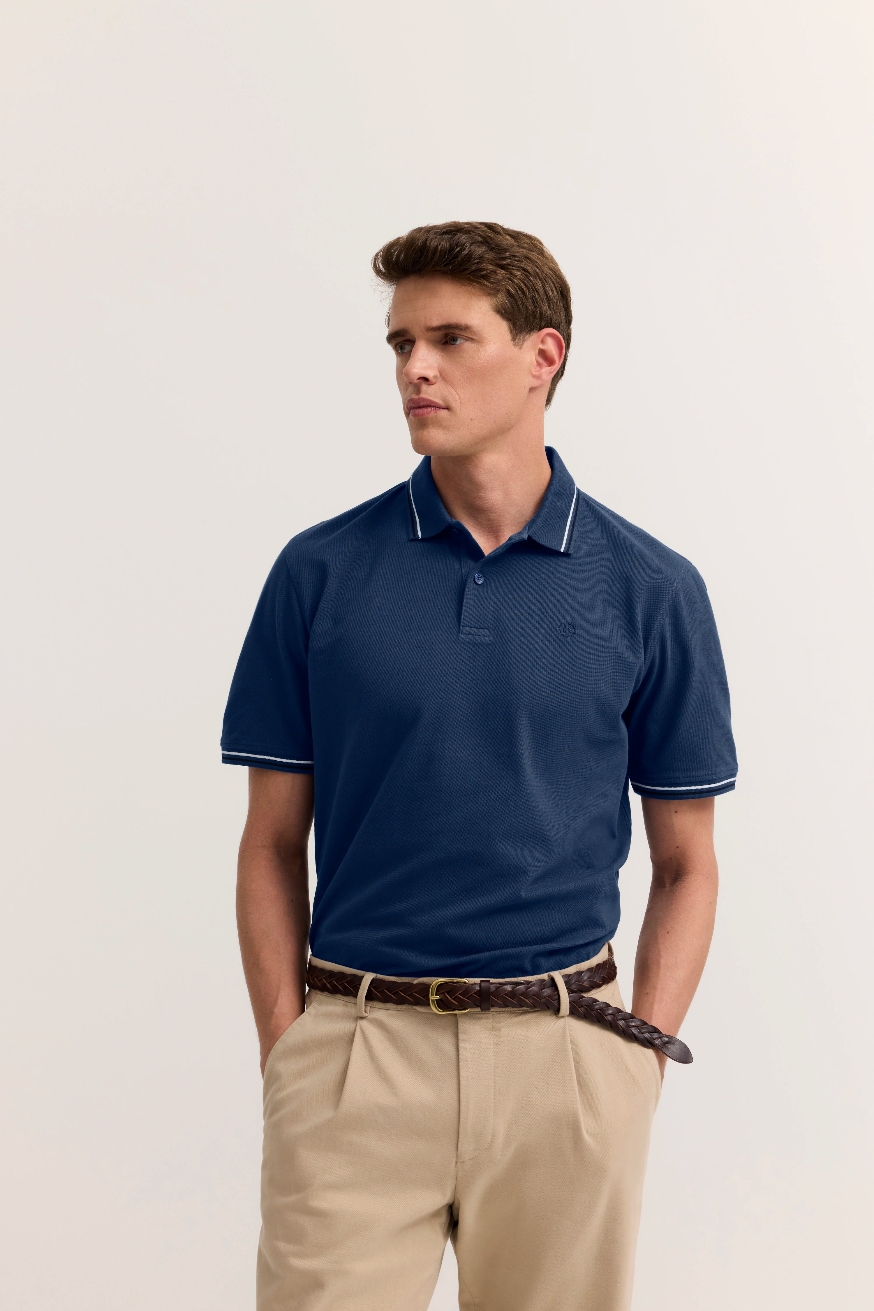 Blaues Polo-Shirt von bugatti, beiges Modellbild, lässige Pose, hochwertig und stilvoll.