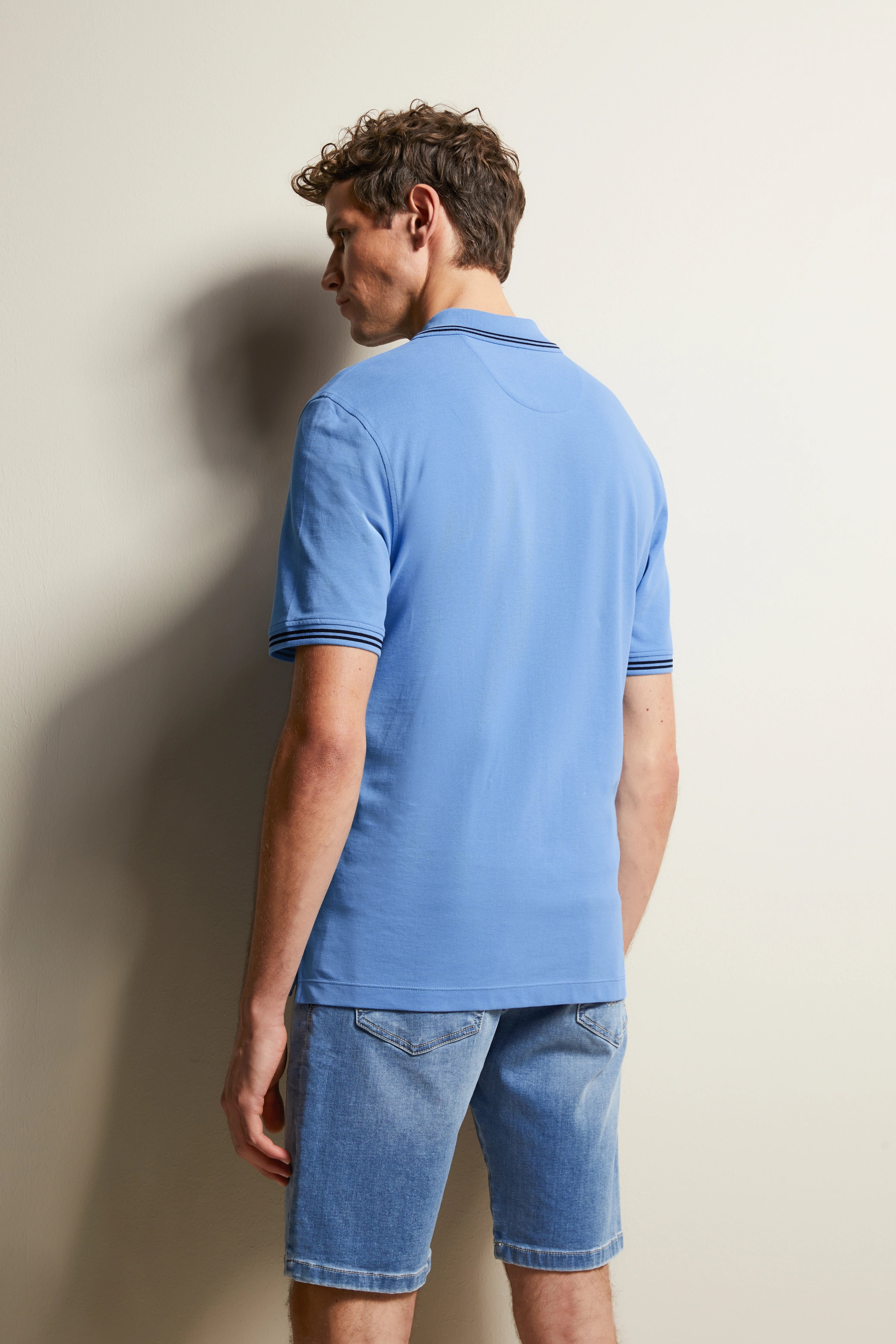 Blue polo shirt and denim shorts, back view, casual model image, relaxed posture.