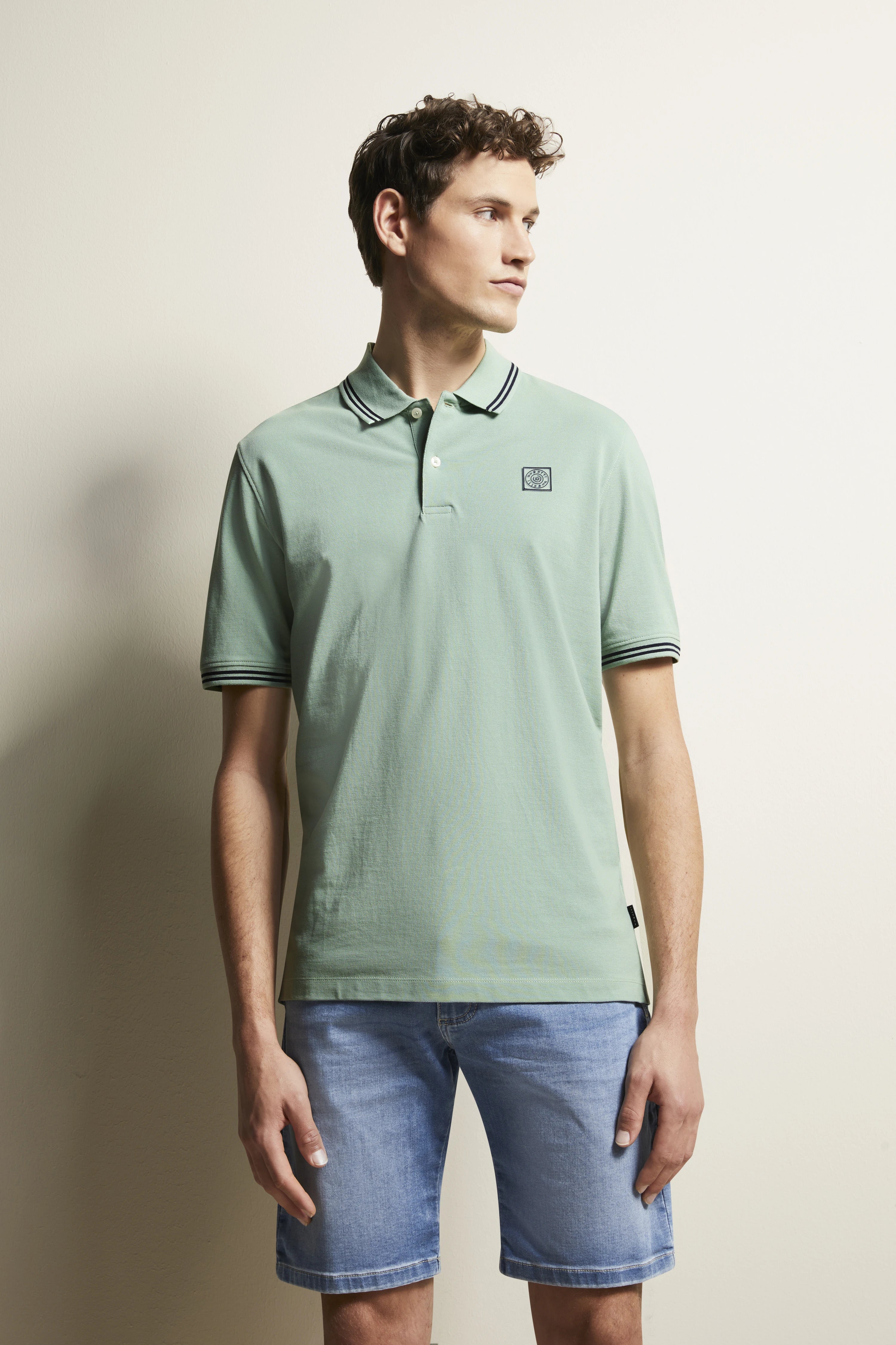 Model wearing mint green polo shirt and blue denim shorts. Casual, side glance. bugatti style.