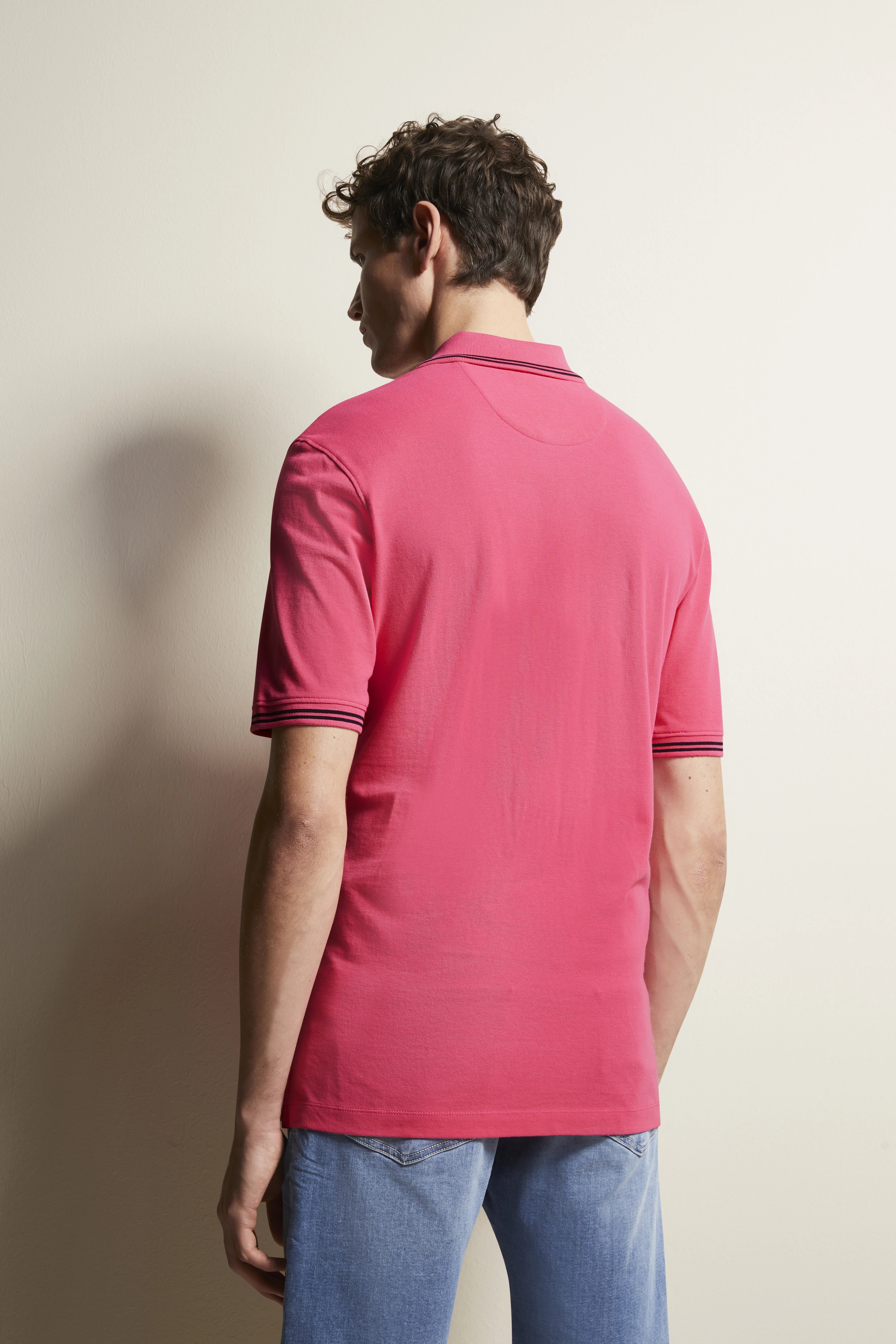 Rear view of model in pink bugatti polo, casually paired with blue jeans. Relaxed pose.