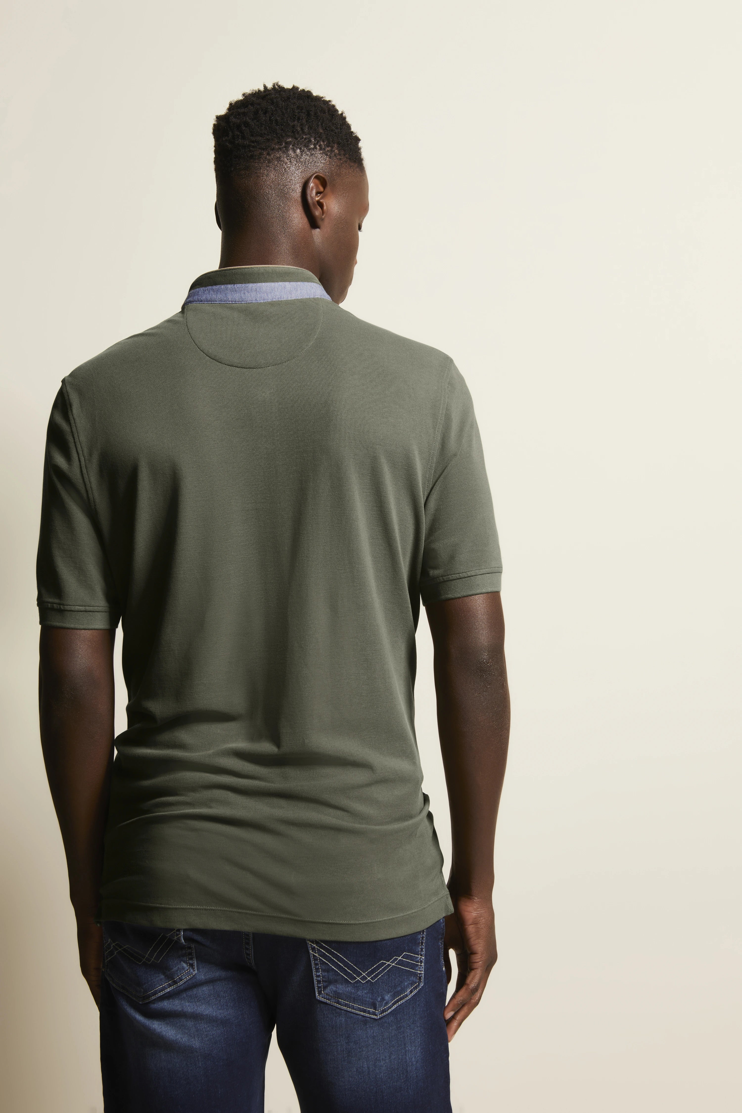 Mann in olivgrünem bugatti Polo und dunkelblauer Jeans, Rückenansicht, legeres Modelbild.