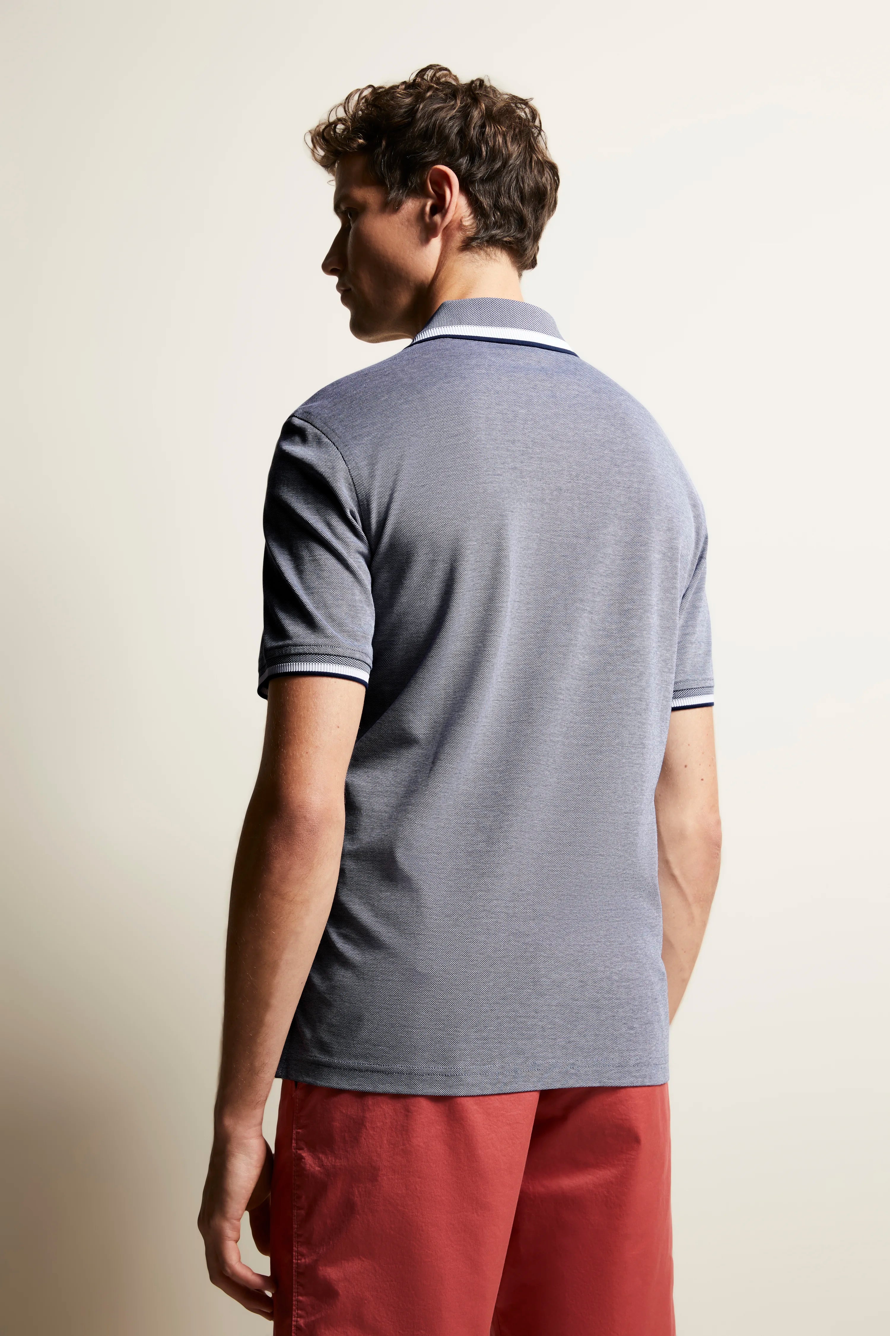 Gray polo shirt and red shorts, model in relaxed pose, back view.