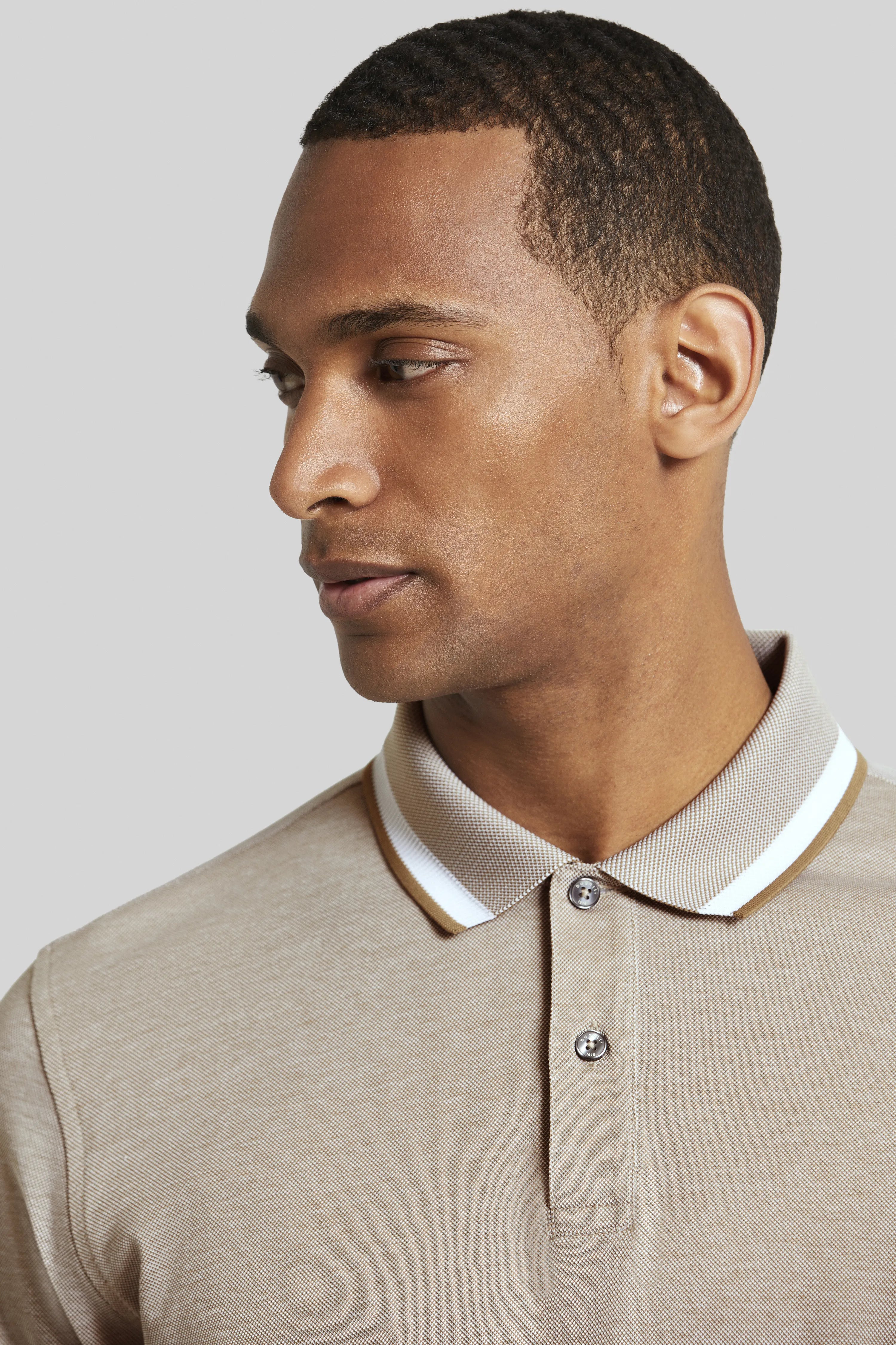 Beiges bugatti Poloshirt auf Model, seitliches Posing, elegante Details, ideal für lässigen Stil.