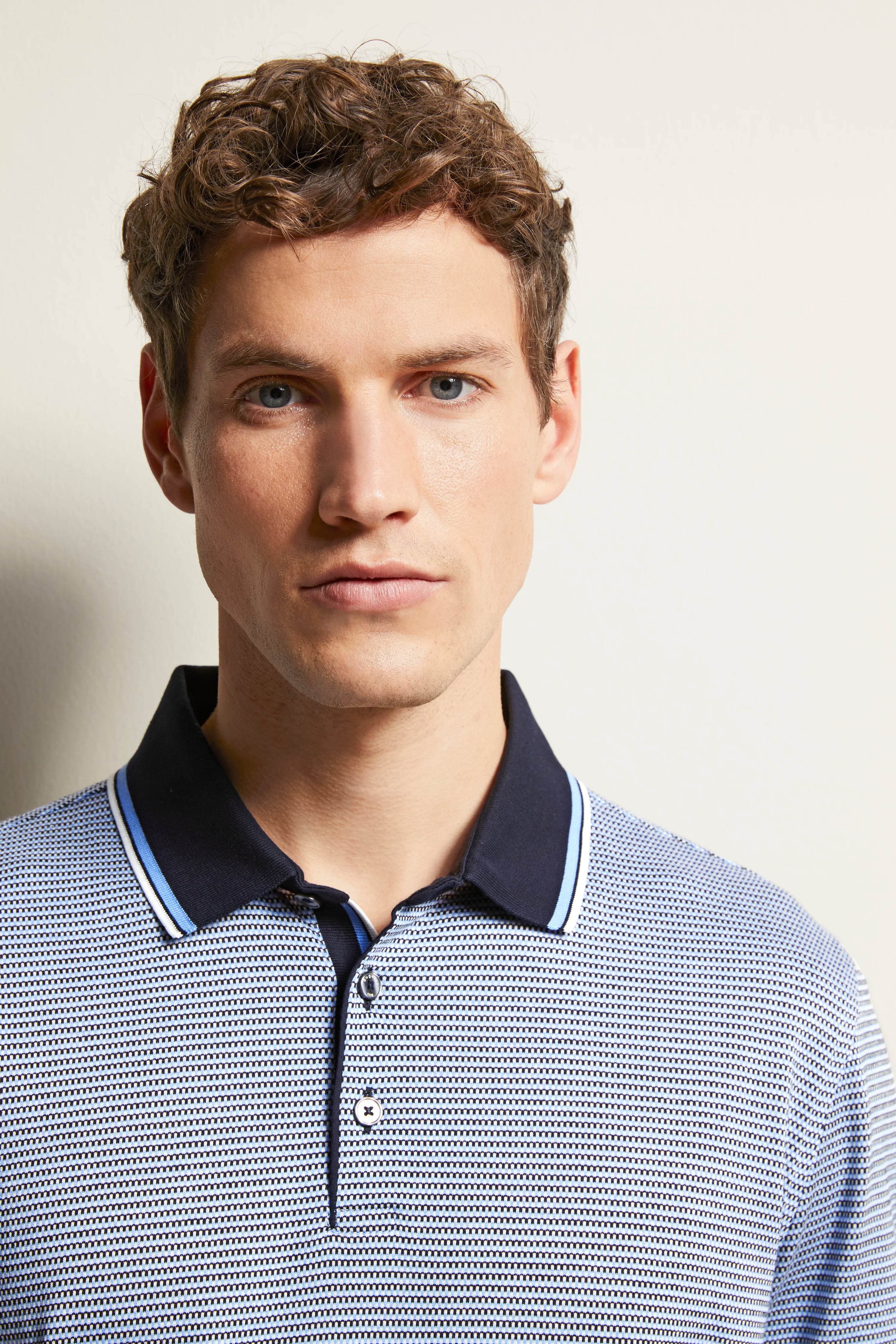Bust of a man in a striped bugatti polo with dark blue collar, elegant and casual.
