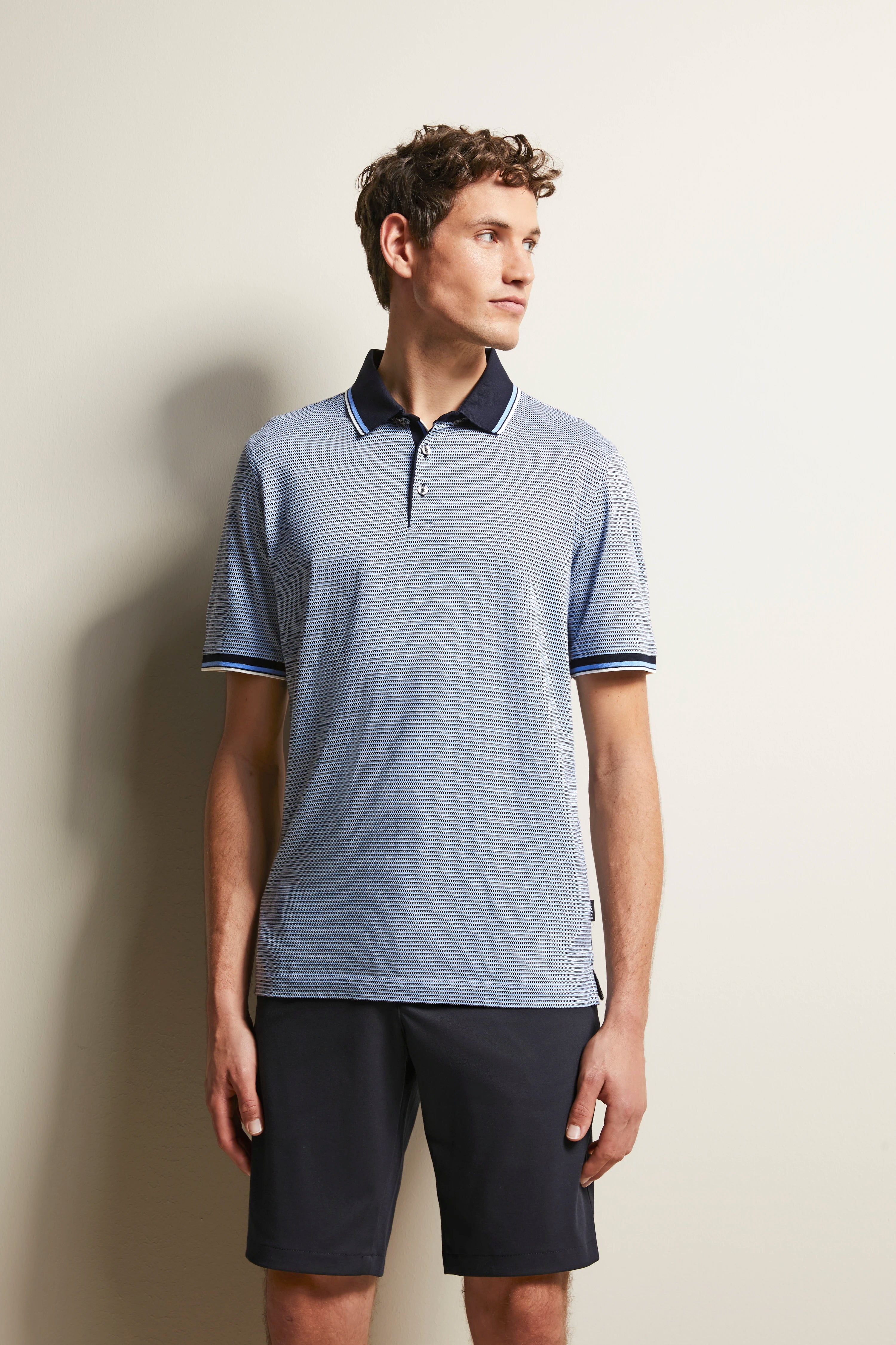 Model wears a striped blue polo shirt with dark blue collar, paired with dark shorts.