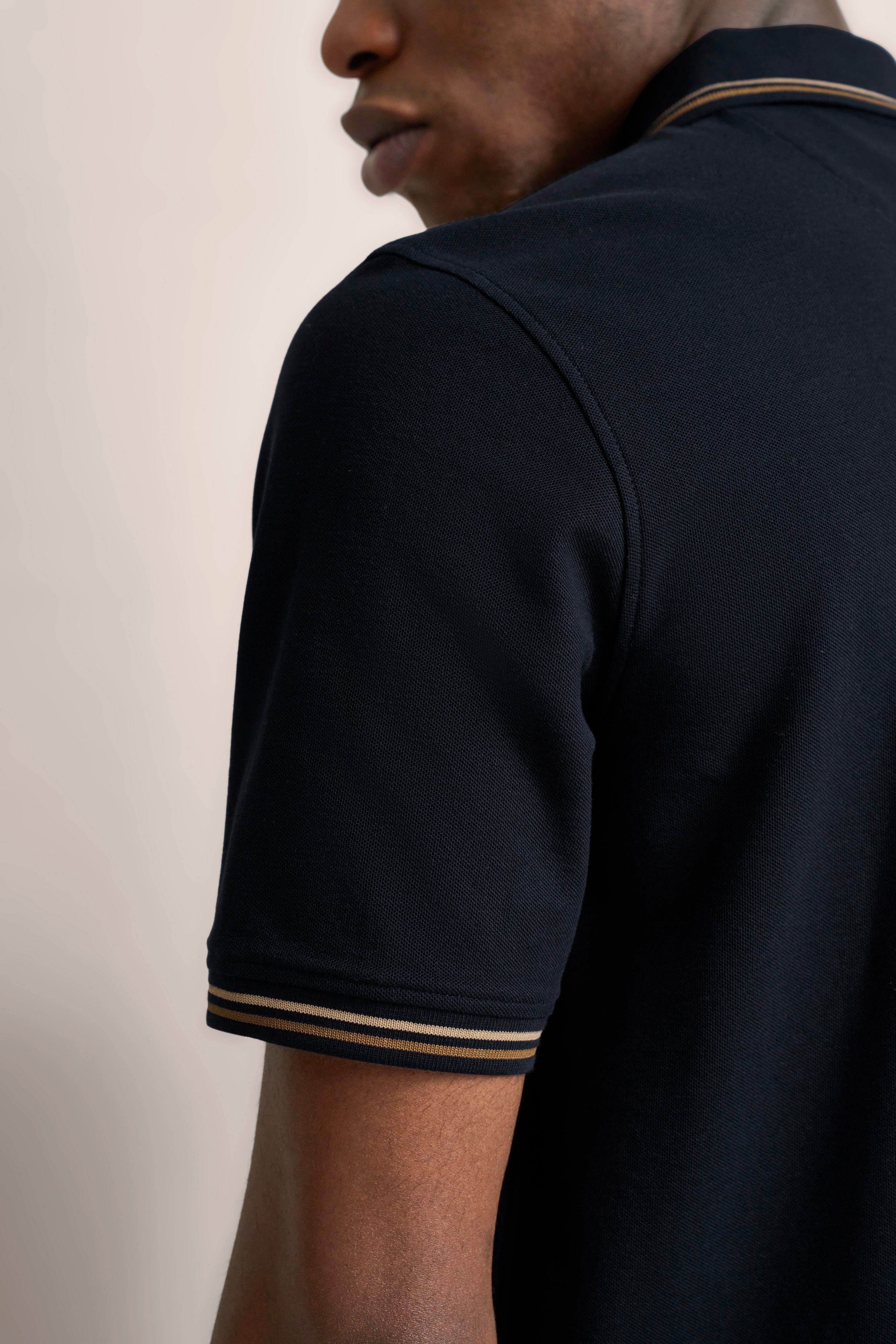 Schwarzes bugatti Poloshirt, gelbe Streifen am Ärmel, Modellaufnahme von der Seite.