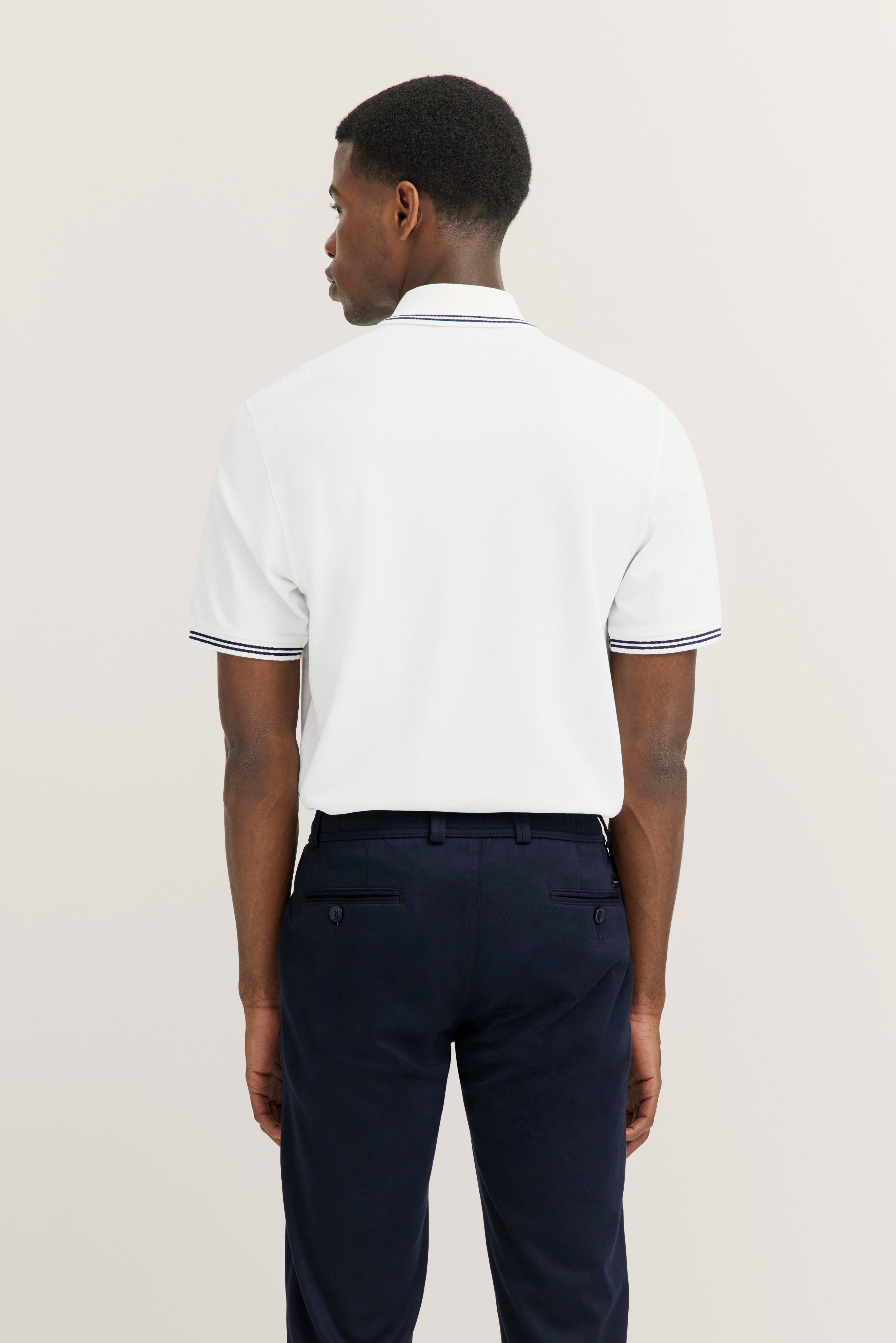 White bugatti polo shirt and dark blue pants, model from behind, relaxed pose.