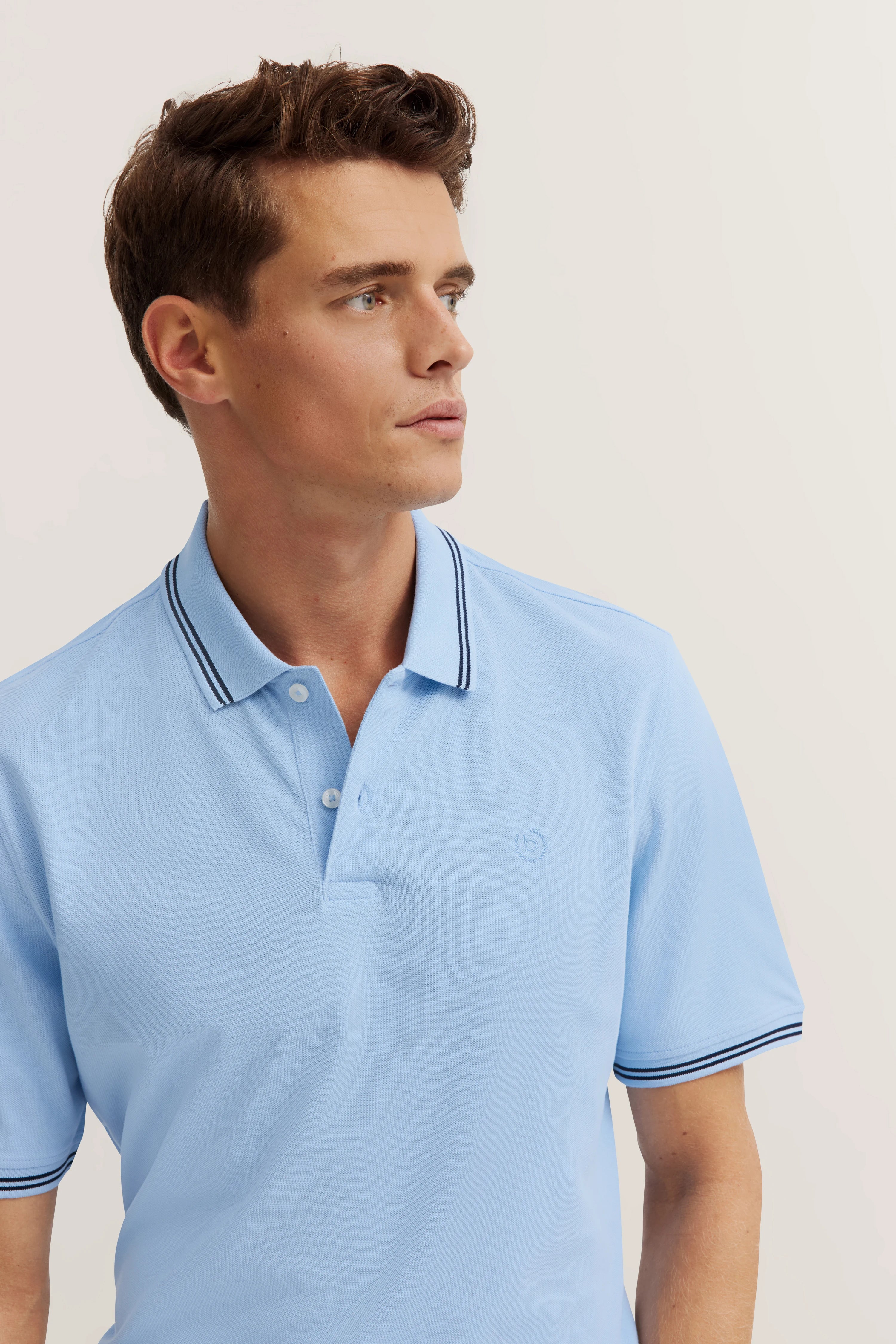 Model in hellblauem bugatti Polohemd mit dunklen Streifen, seitliches Posing.