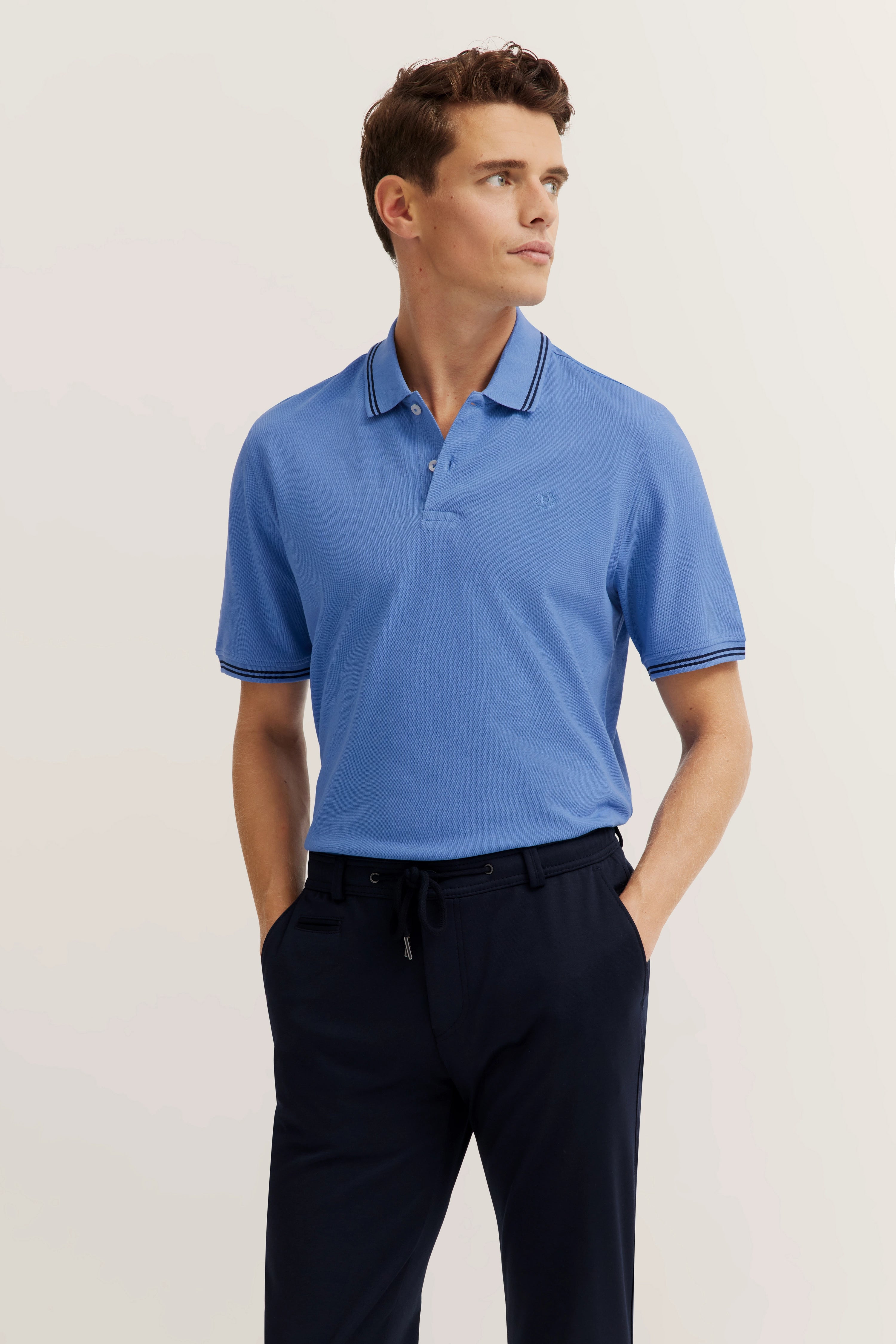 Model trägt blaues bugatti Poloshirt und schwarze Hose. Legeres Posing, Blick zur Seite.