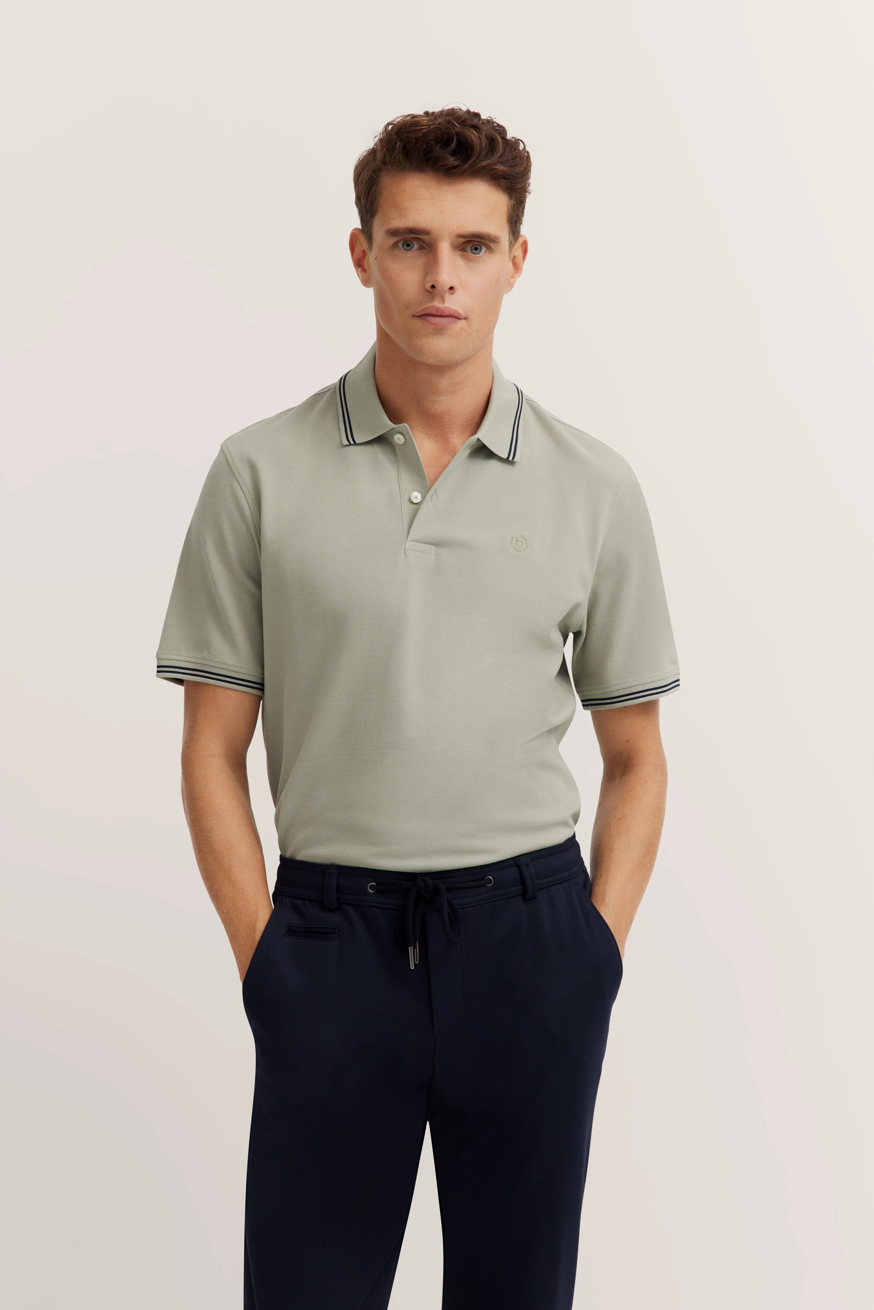 bugatti Modelbild: graues Polohemd, dunkelblaue Hose, entspanntes Posing.
