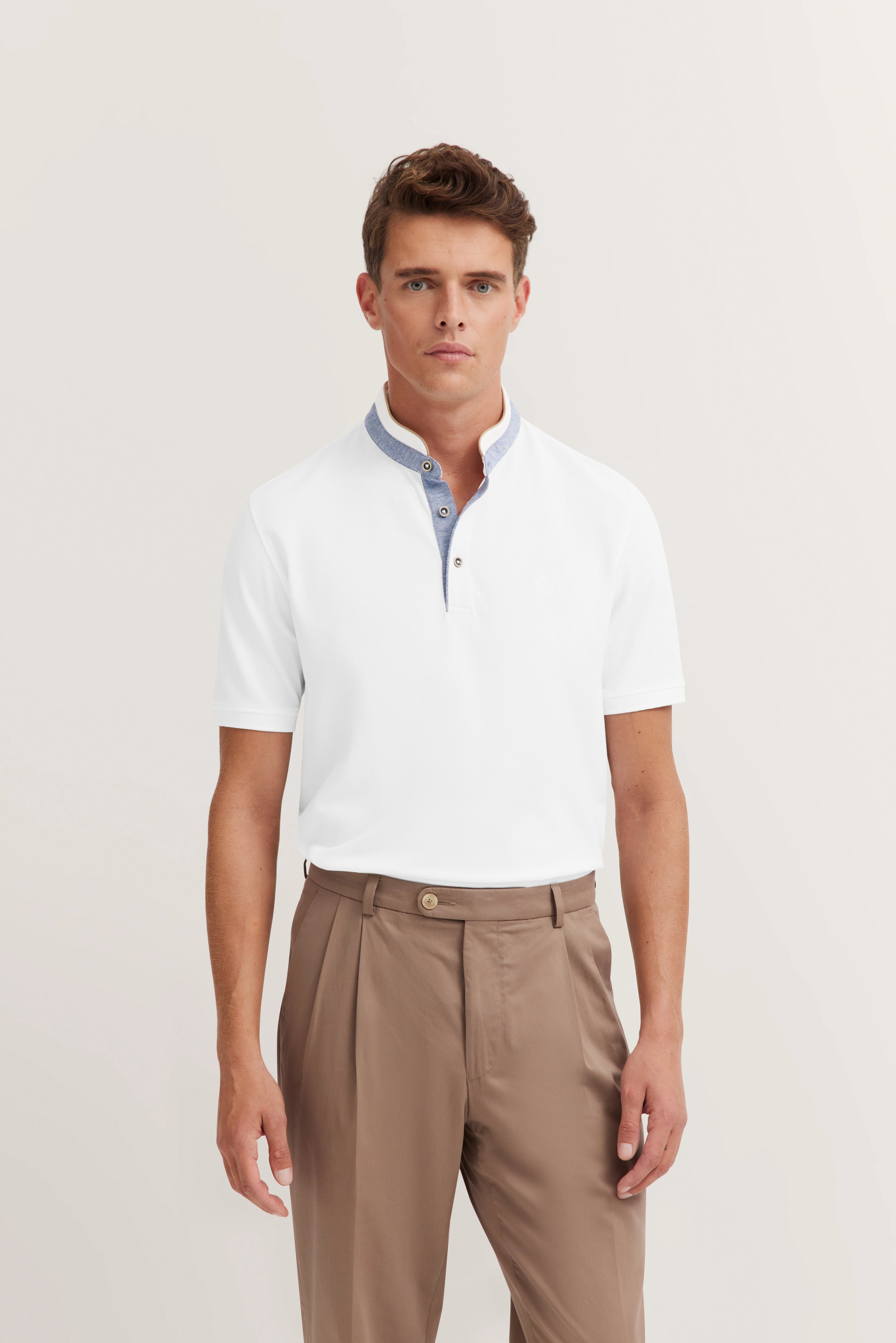 Weißes Polohemd mit blauem Kragen, beigefarbene Hose, Model frontal stehend.