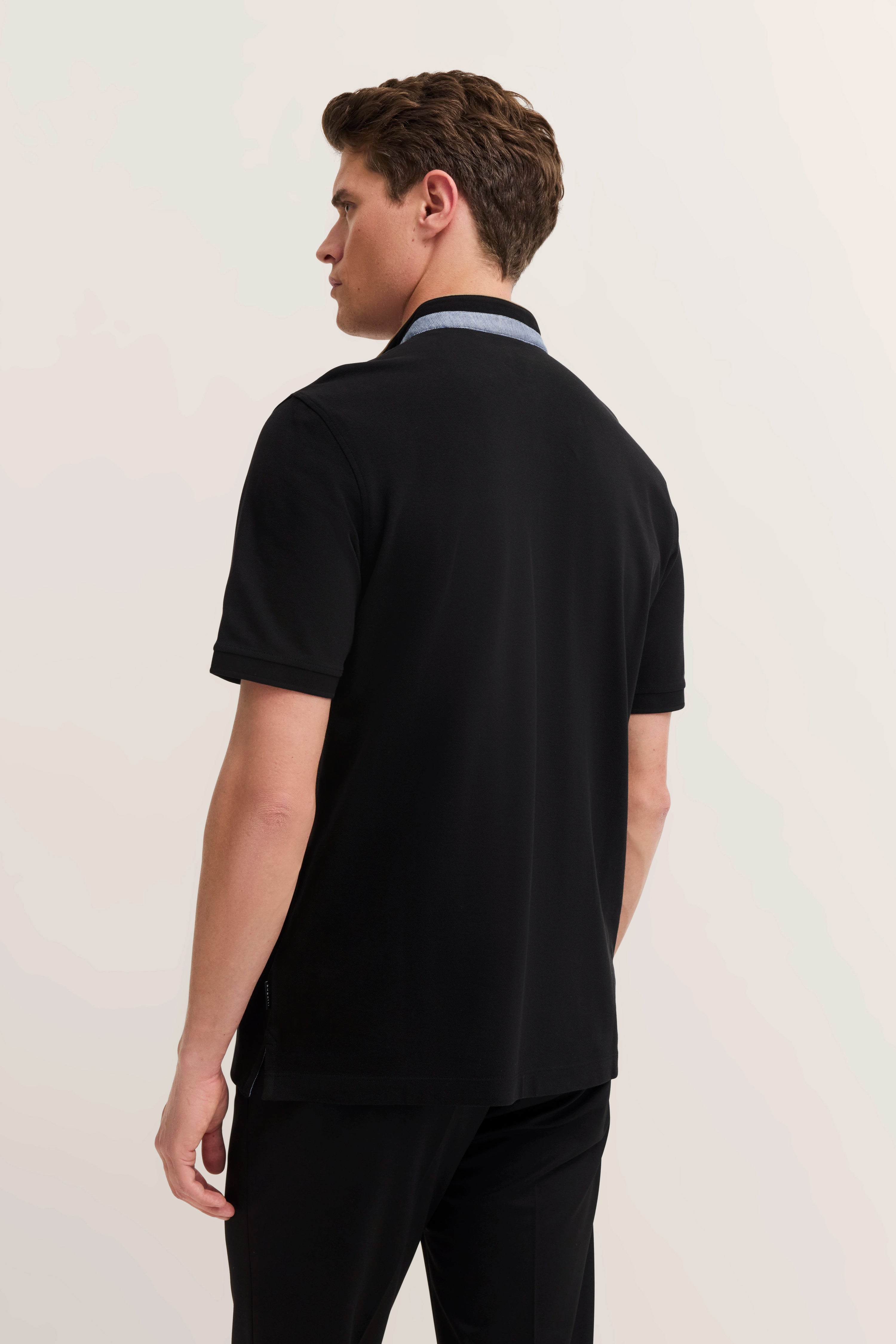 Male model in black bugatti polo shirt, side pose, relaxed stance.