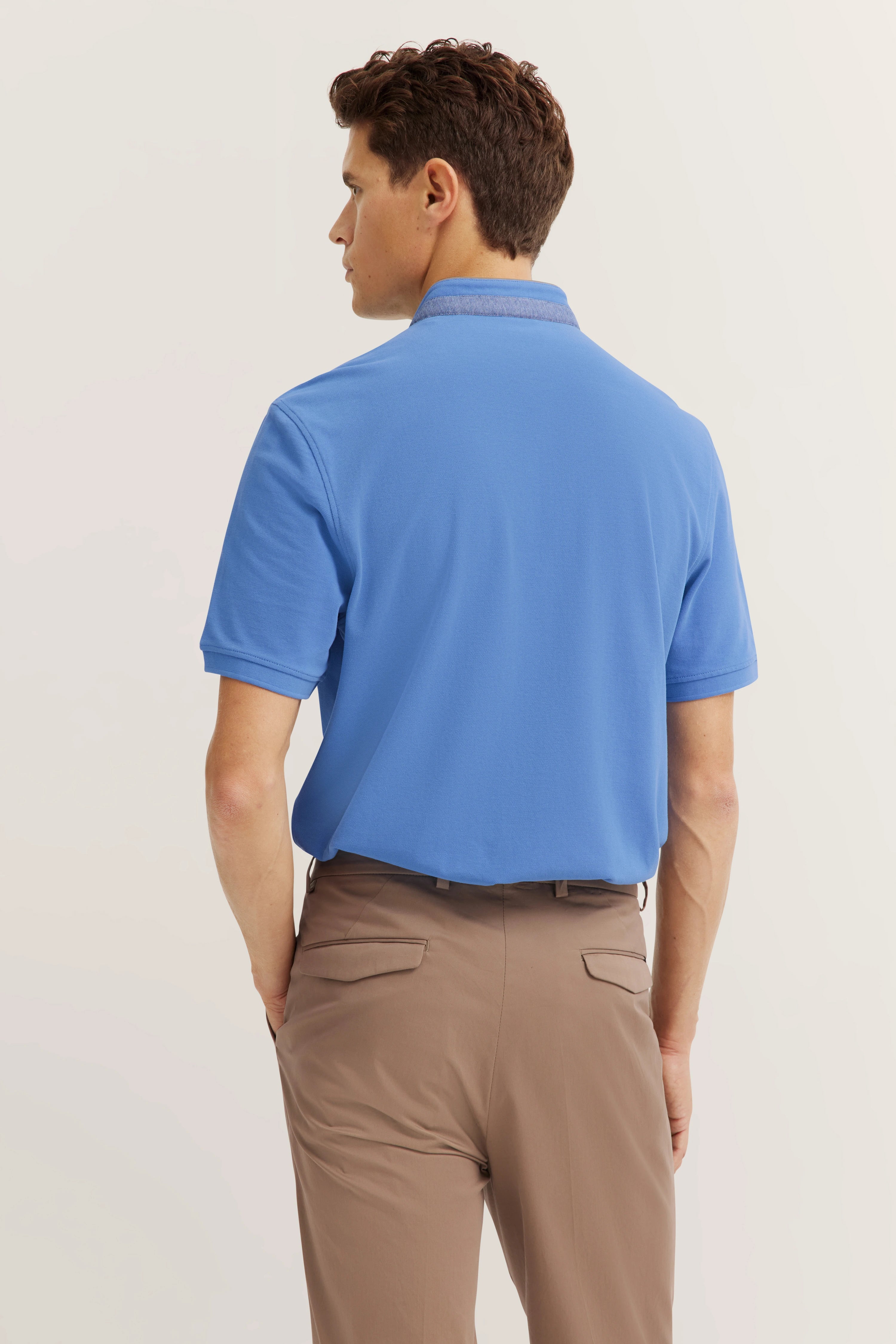 Back view of model in blue polo shirt and beige pants, relaxed pose, embodying bugatti's refined and timeless style.