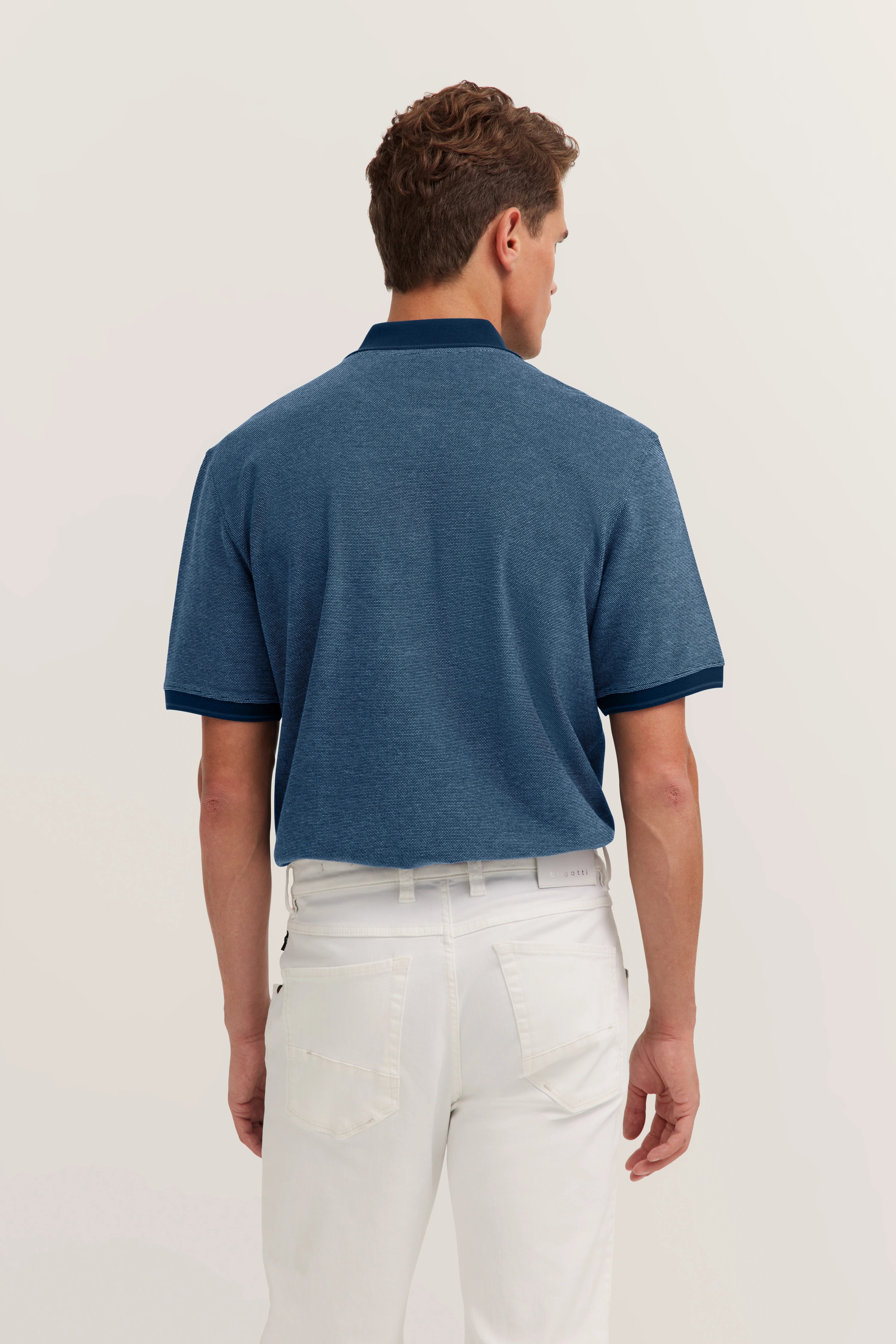 Model in blue polo shirt and white jeans, back view, casual pose.