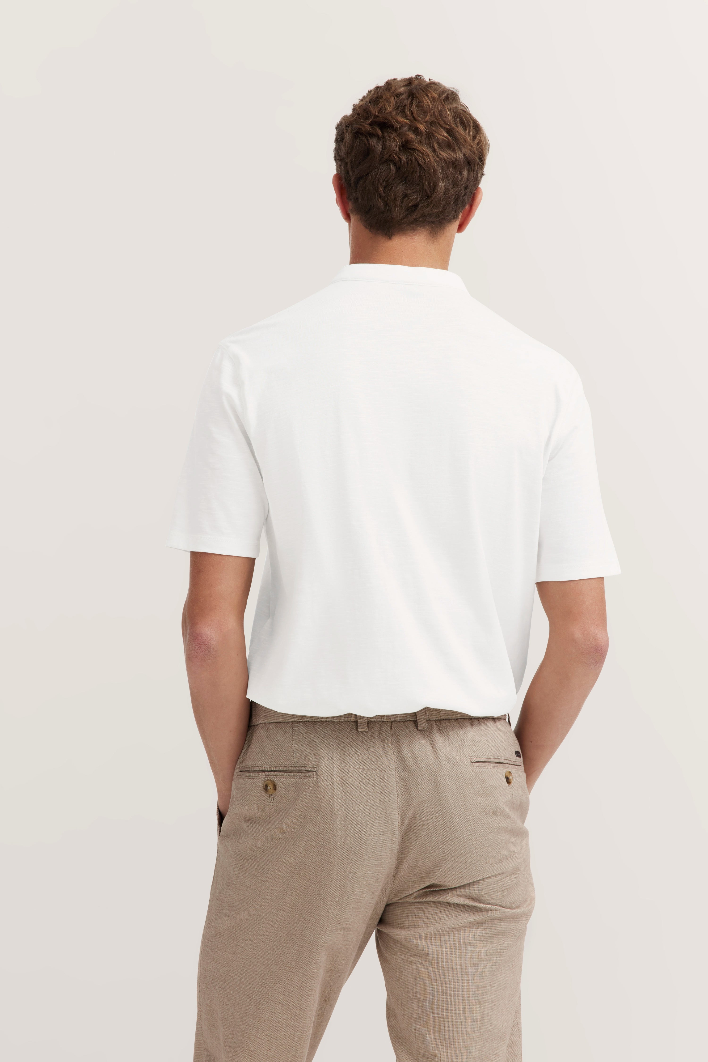 White bugatti polo shirt, beige pants, model rear view, relaxed pose.
