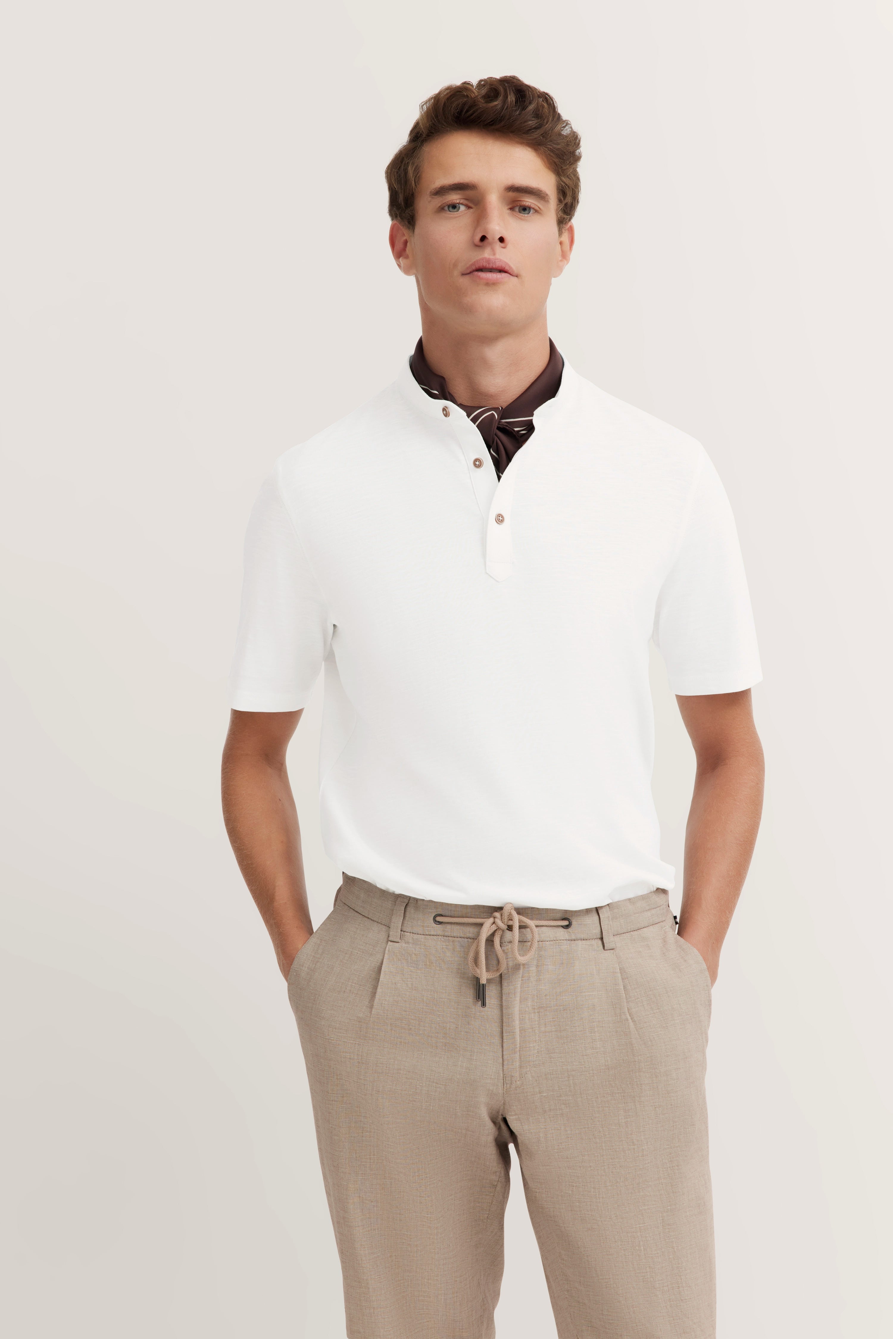 White polo shirt & beige trousers, model in relaxed pose with hands in pockets, embodying bugatti's refined style.