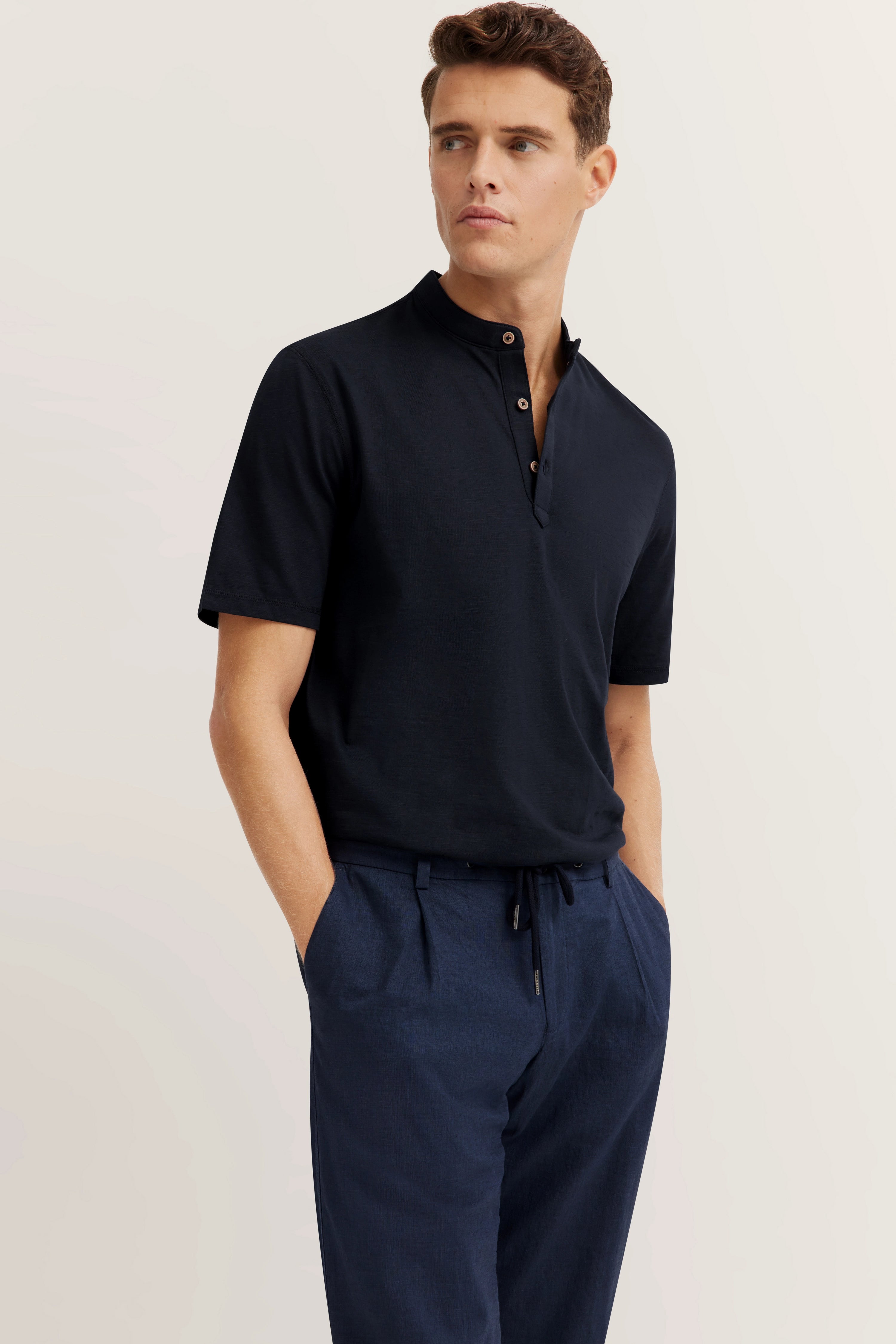 Model trägt dunkelblaues bugatti Poloshirt und Hose, legeres Posing, Hände in Hosentaschen.