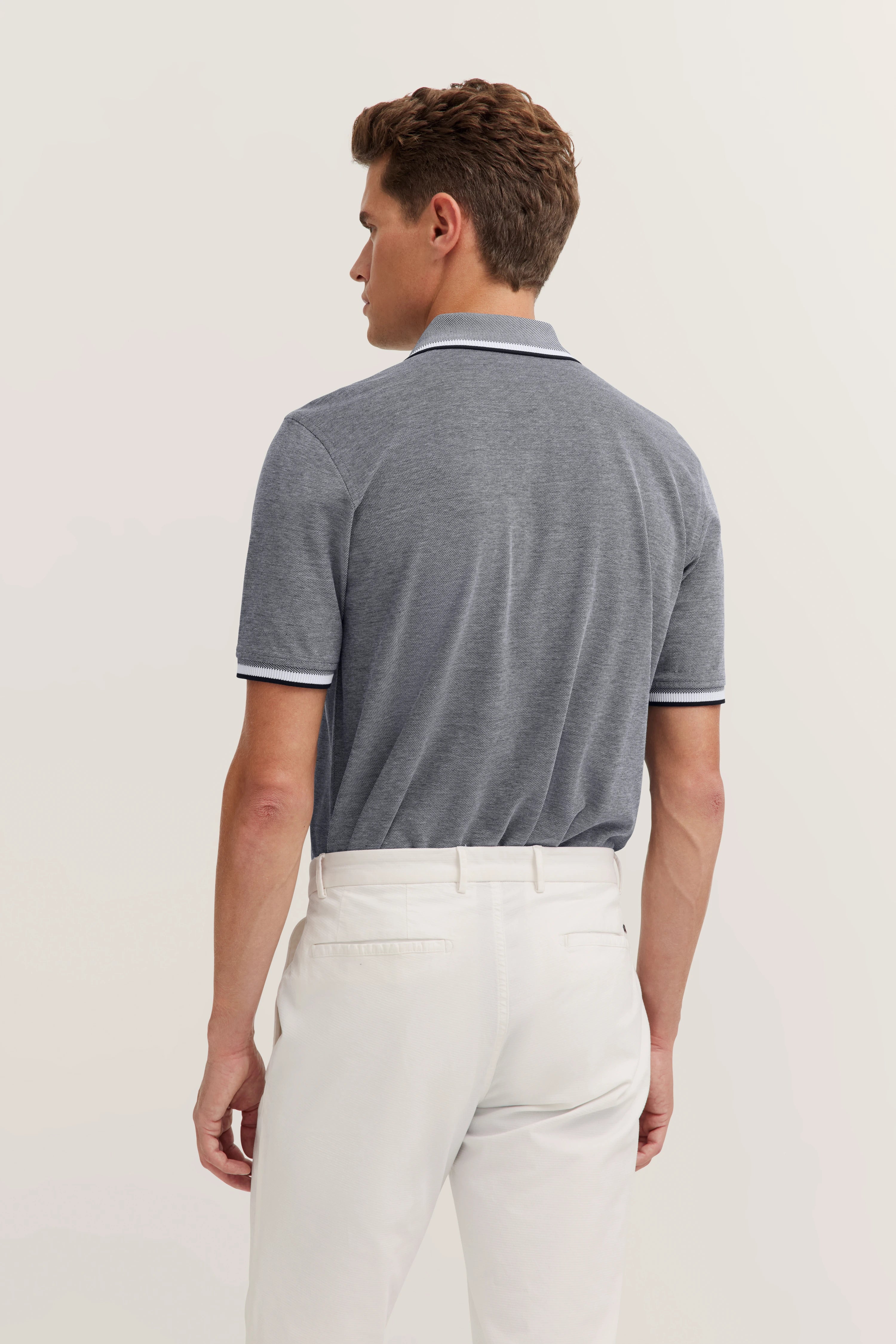 bugatti grey polo shirt, white trousers, back view, model in relaxed pose, style and sophistication inspire.