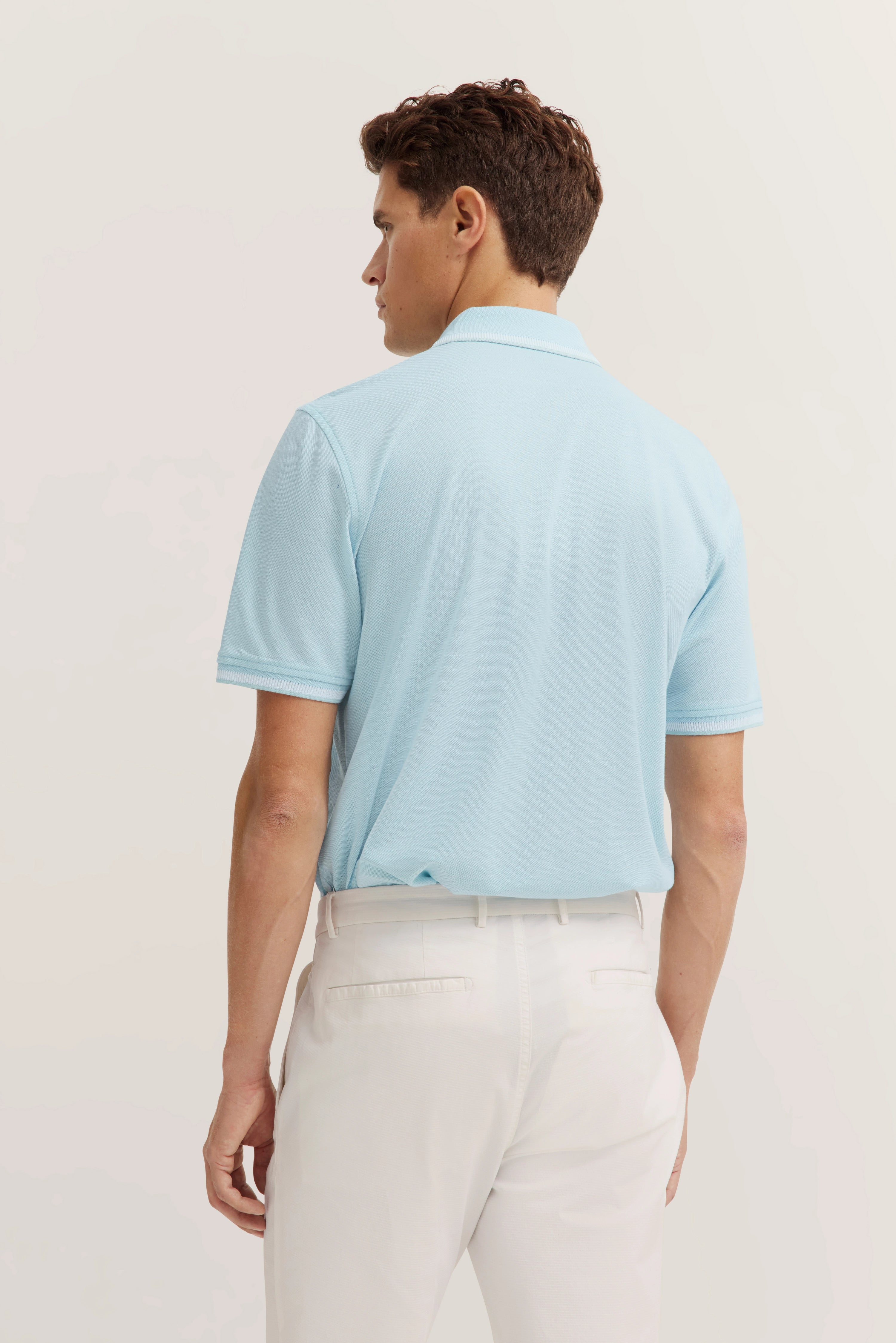 bugatti model in light blue polo shirt and white trousers, back view.