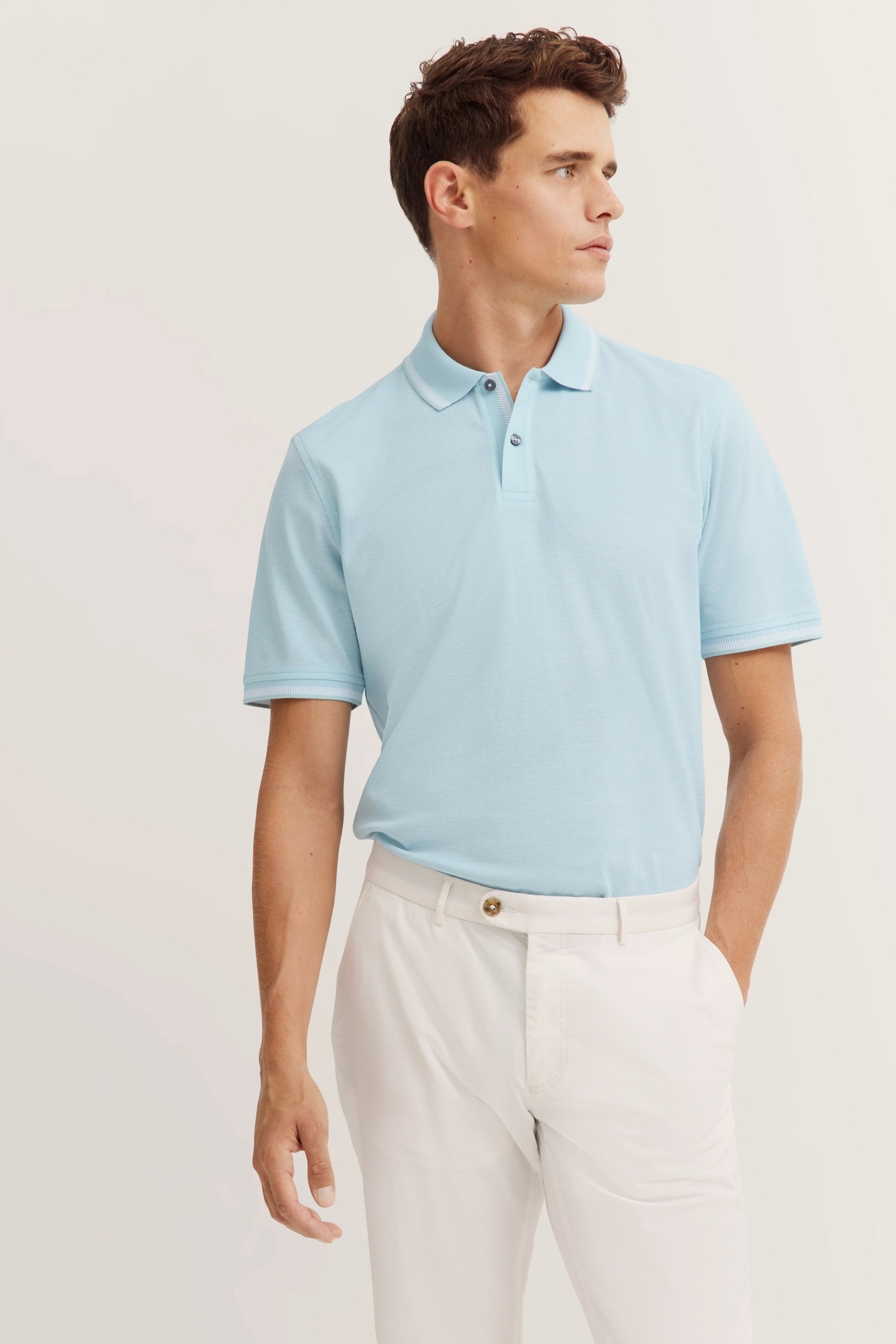 Model in light blue polo and white pants by bugatti, posing with relaxed elegance.