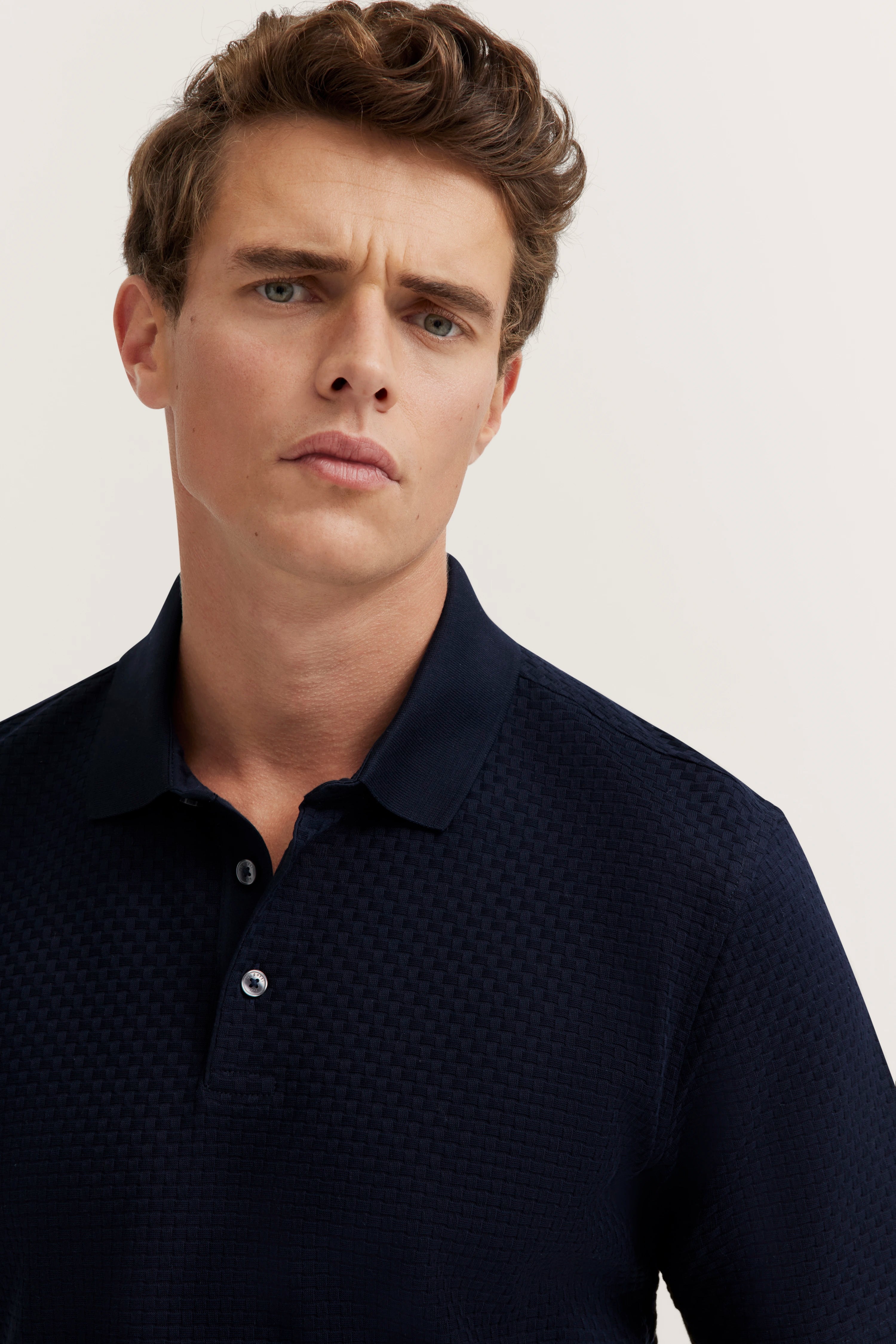 Bust of a man in a dark blue bugatti polo shirt with textured pattern.