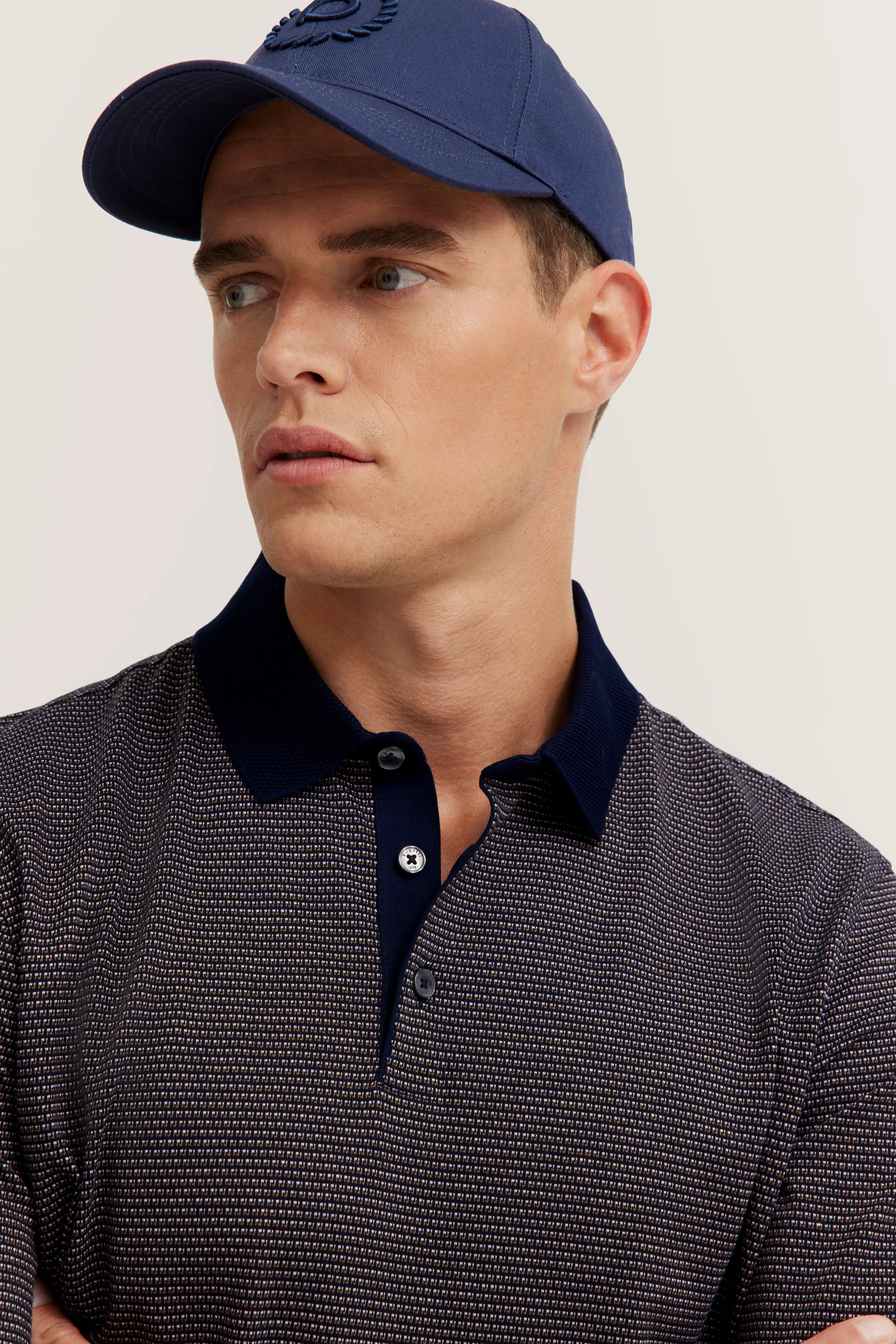 Model wearing blue bugatti patterned polo and cap, bust shot, relaxed expression.