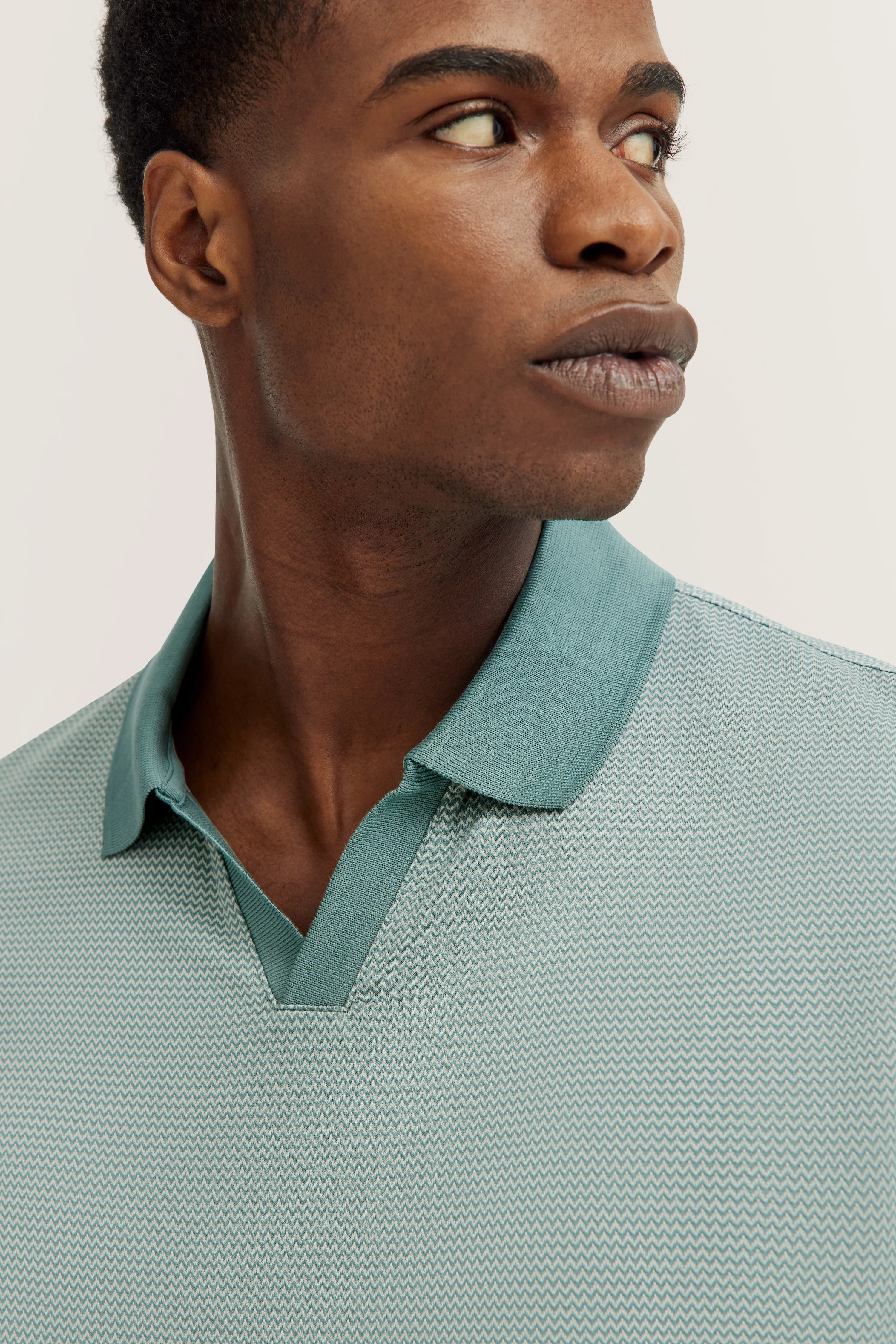 Model wears mint bugatti polo shirt with zigzag pattern, bust view, looking sideways.