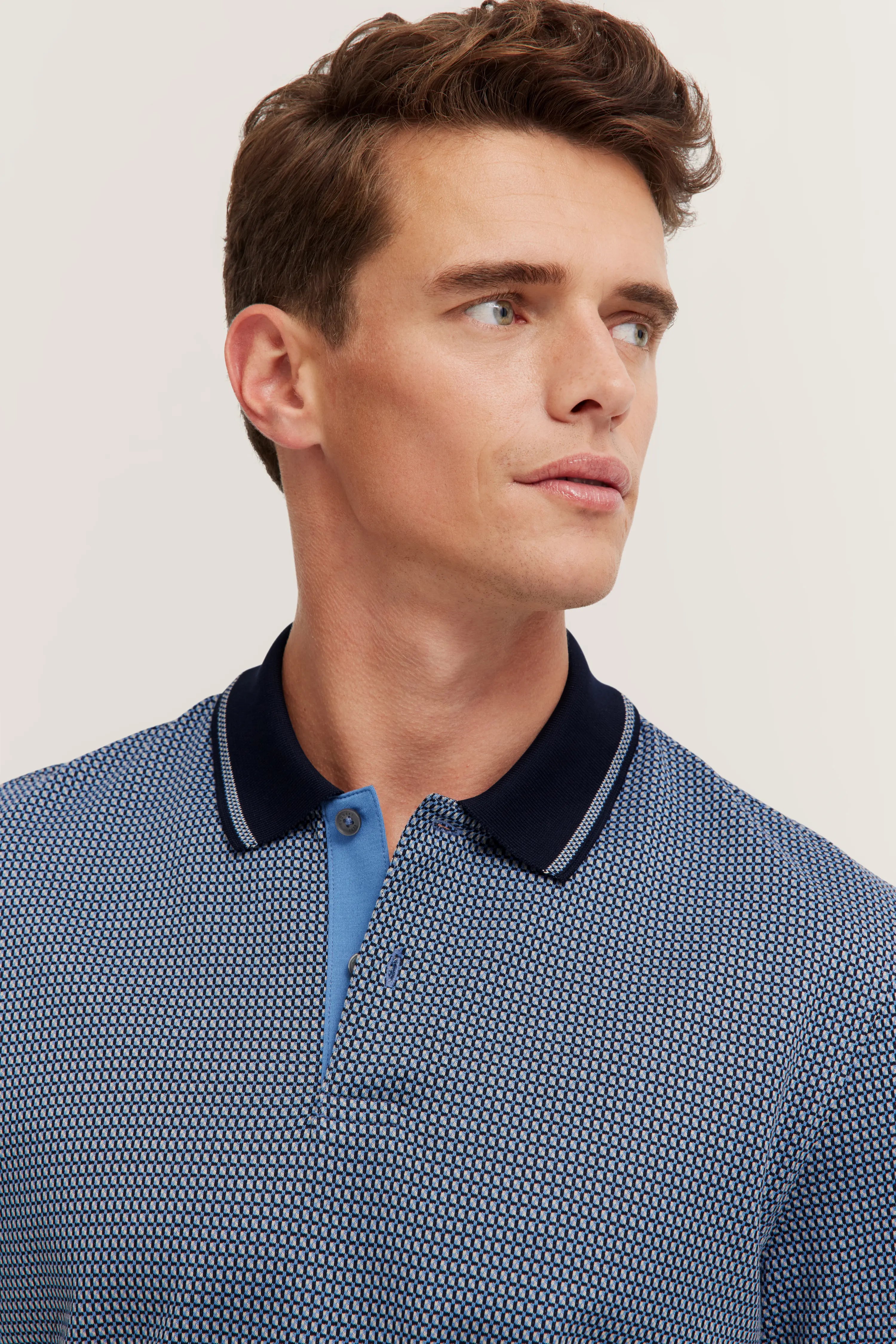 Blue patterned polo shirt with dark collar, model turned sideways.
