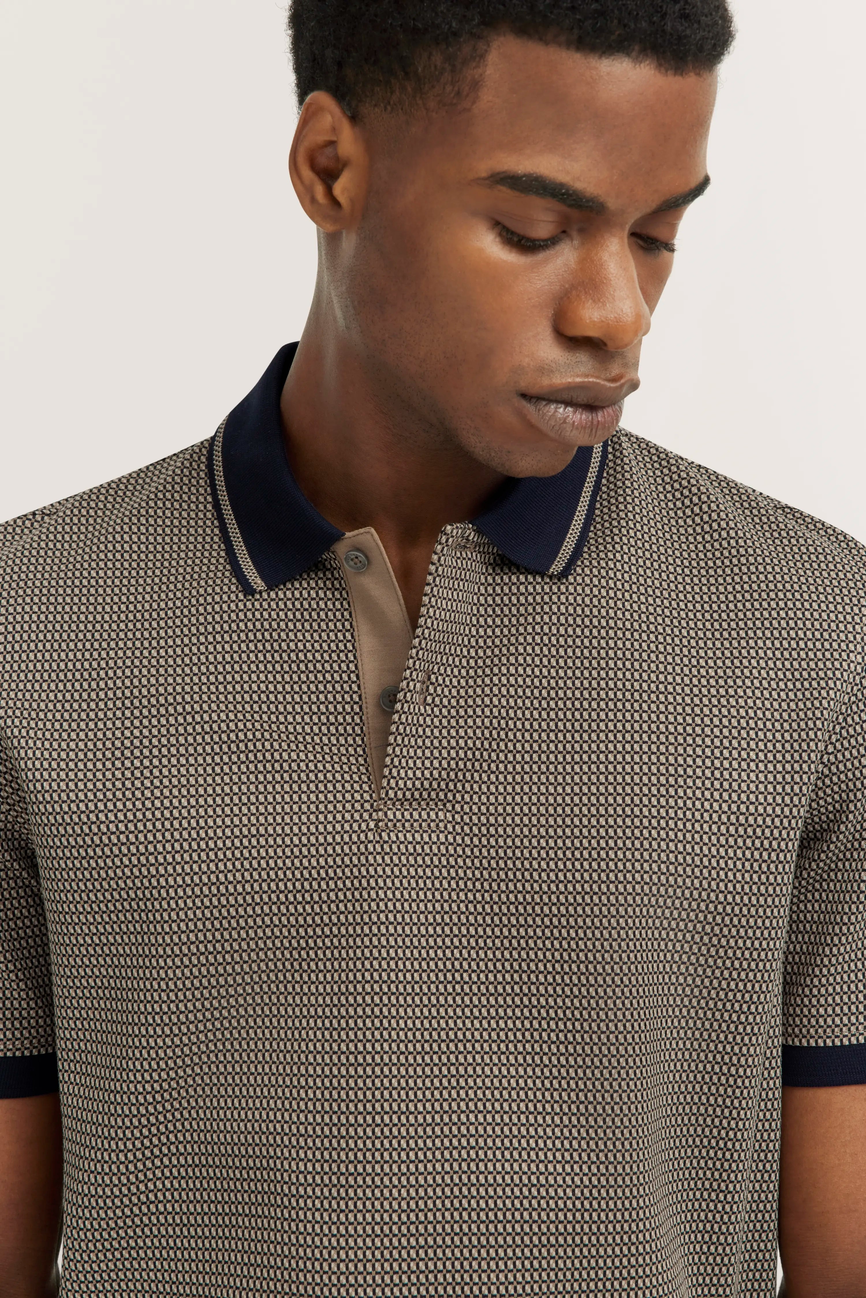 Poloshirt with geometric pattern in beige and navy, model in half-profile, relaxed expression.