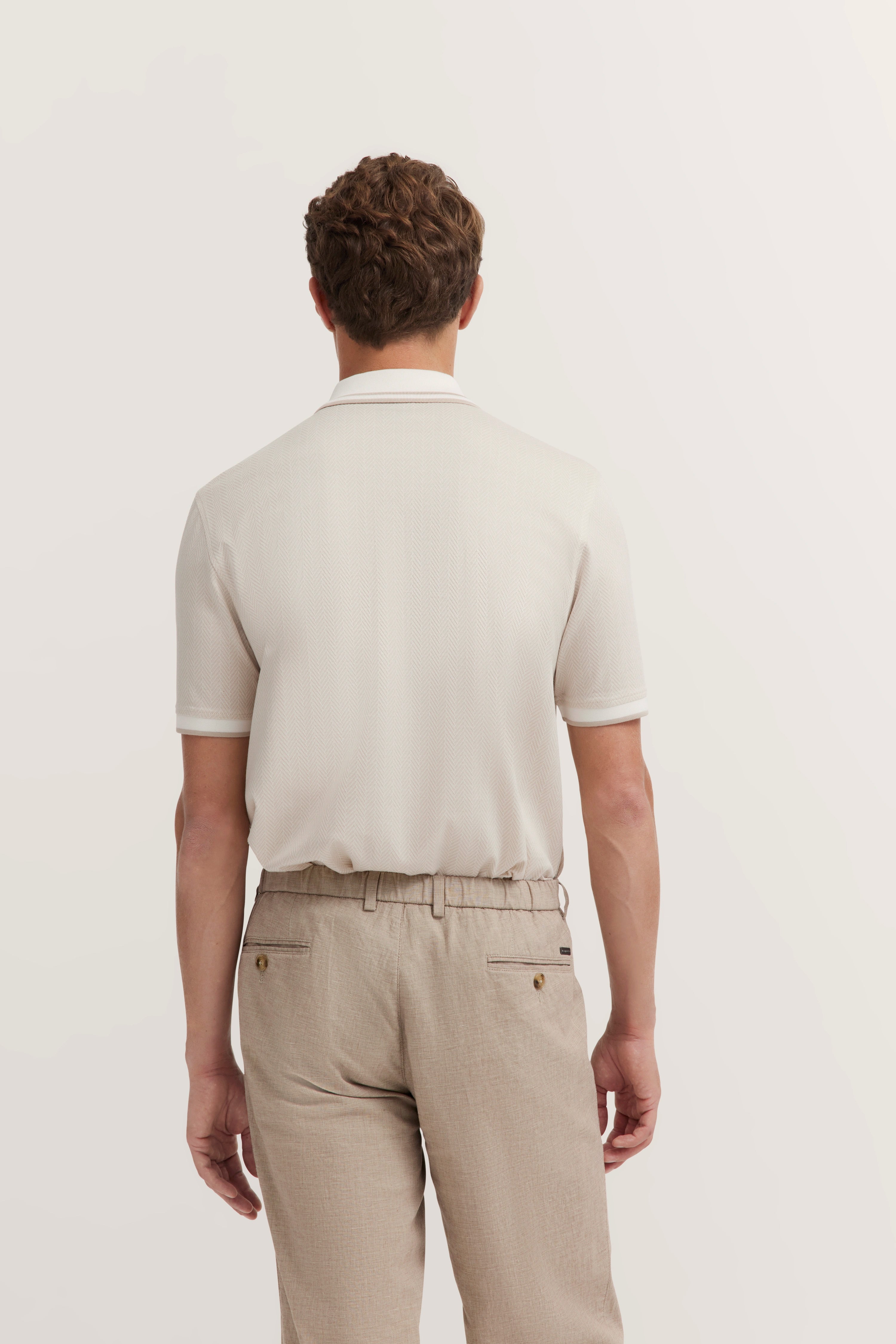 Beige polo shirt and light pants, back view on model, relaxed pose, embodying bugatti's timeless elegance and style.