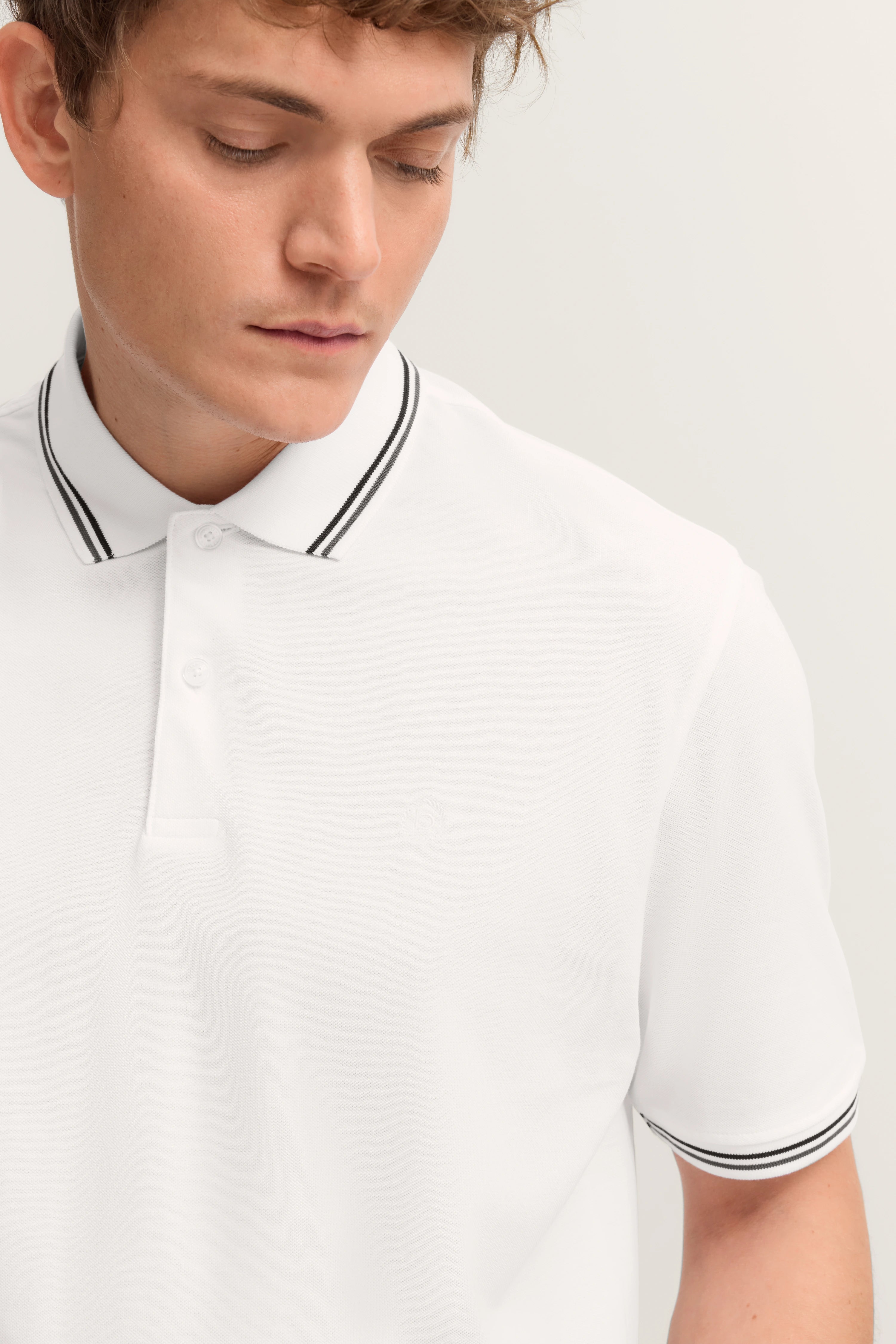 Weiße bugatti Poloshirt mit schwarzen Streifen am Kragen, Modelbild, Kopf leicht geneigt.