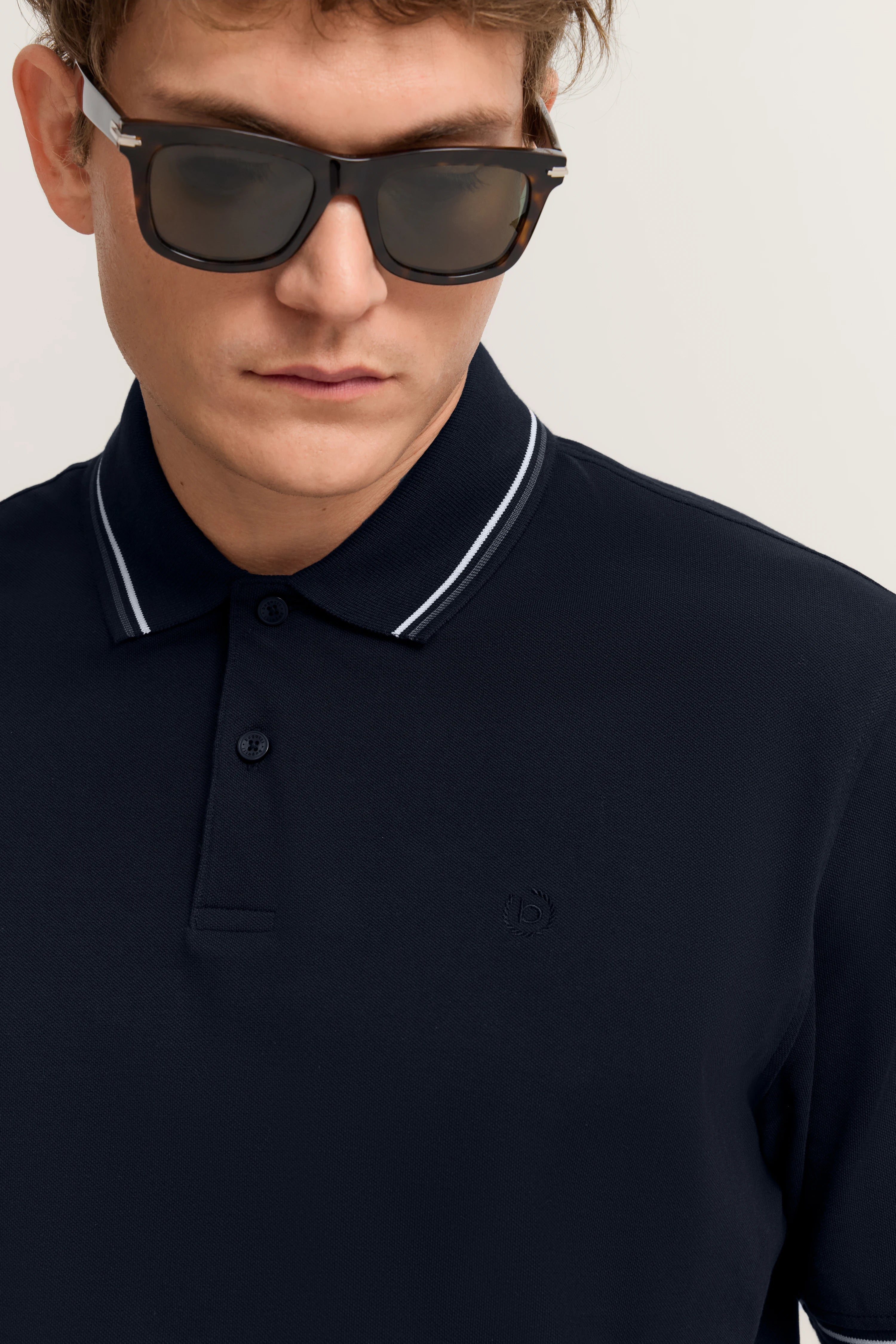 Dunkelblaues Polohemd von bugatti, getragen von einem Model mit Sonnenbrille, Nahaufnahme.