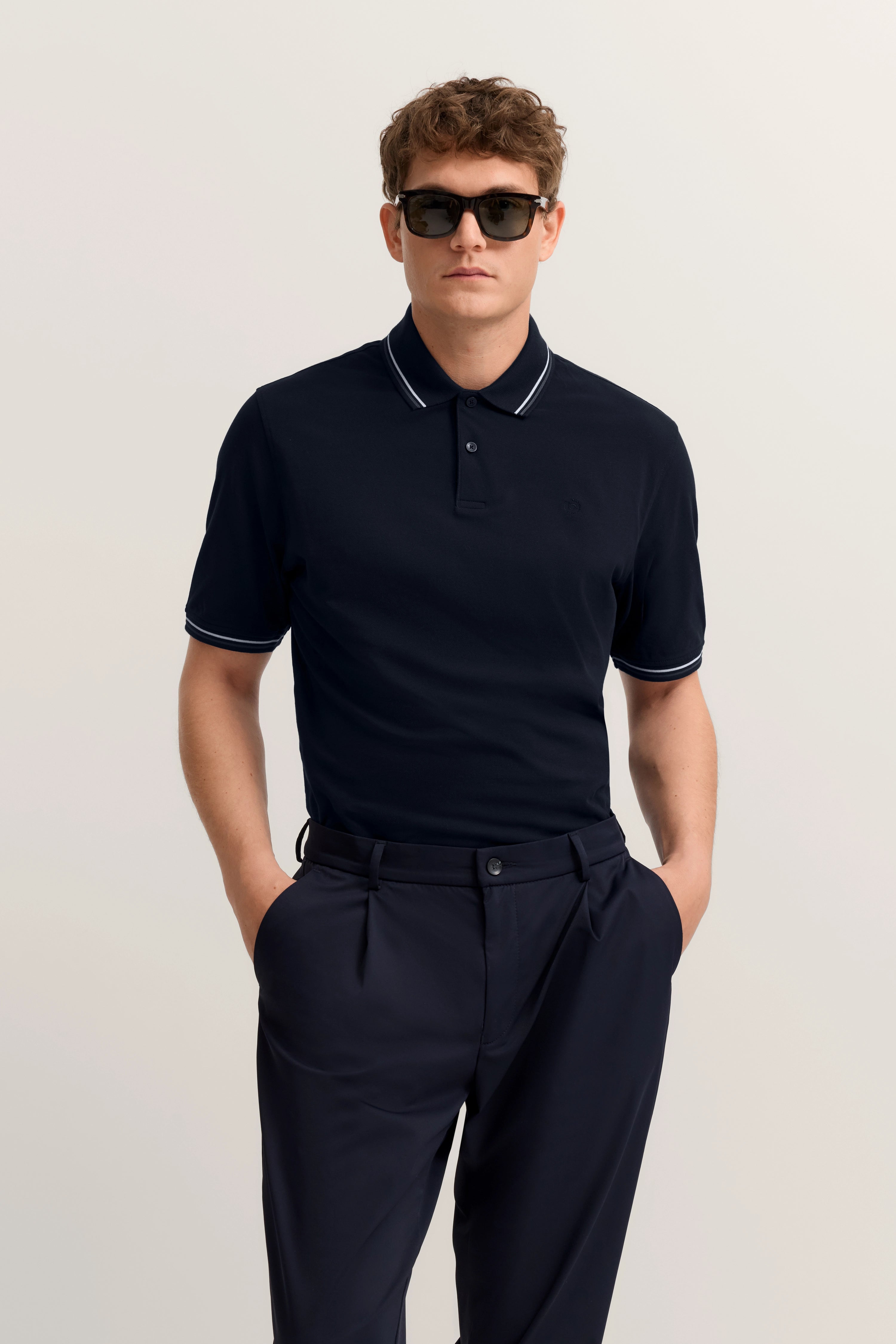 bugatti Model in navy Polo und Hose, legeres Posing, Hände in den Taschen, stilvoll und entspannt.