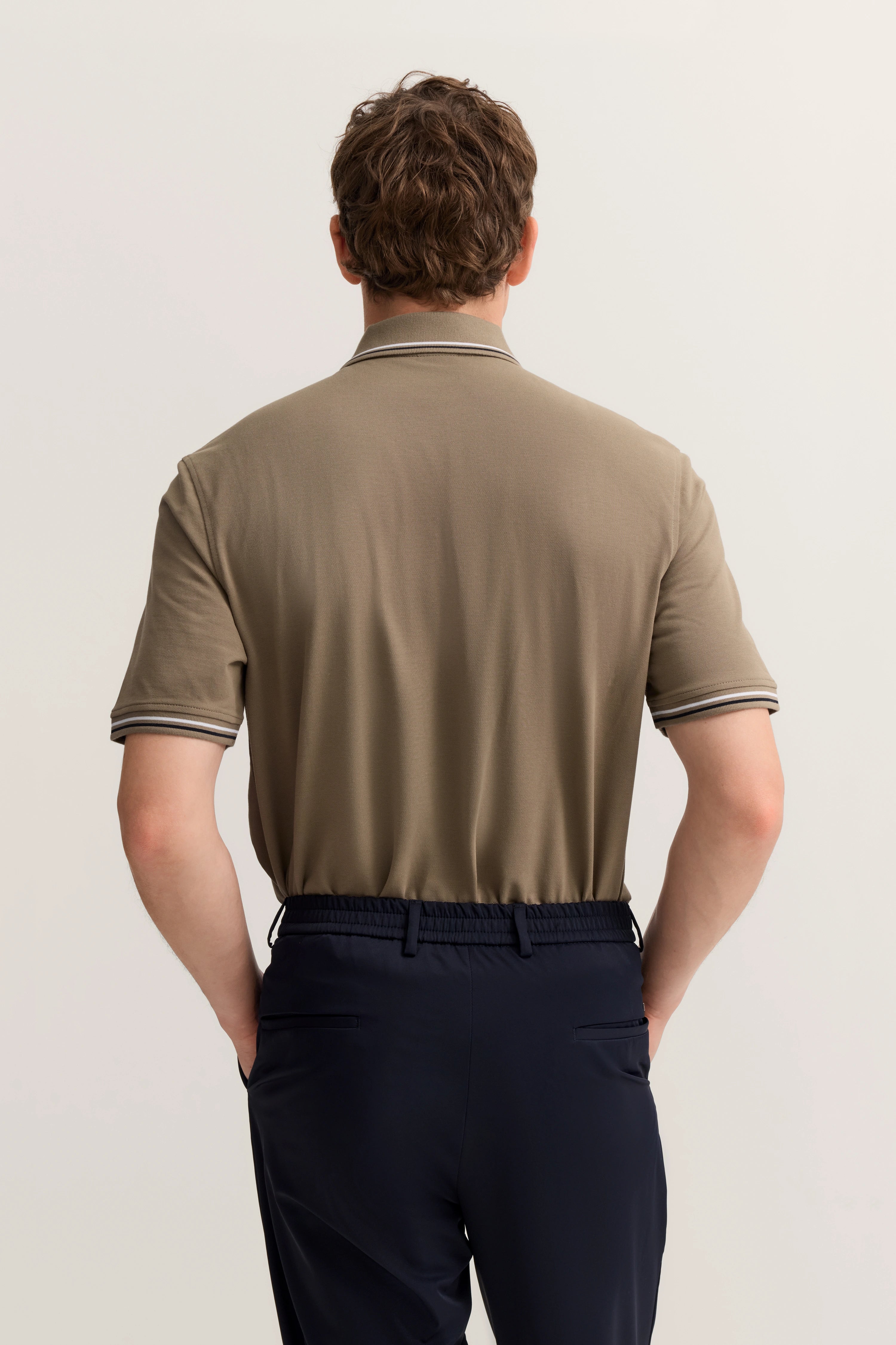 Braunes Polo-Shirt und blaue Hose von hinten, legeres Modelbild, entspannte Haltung.