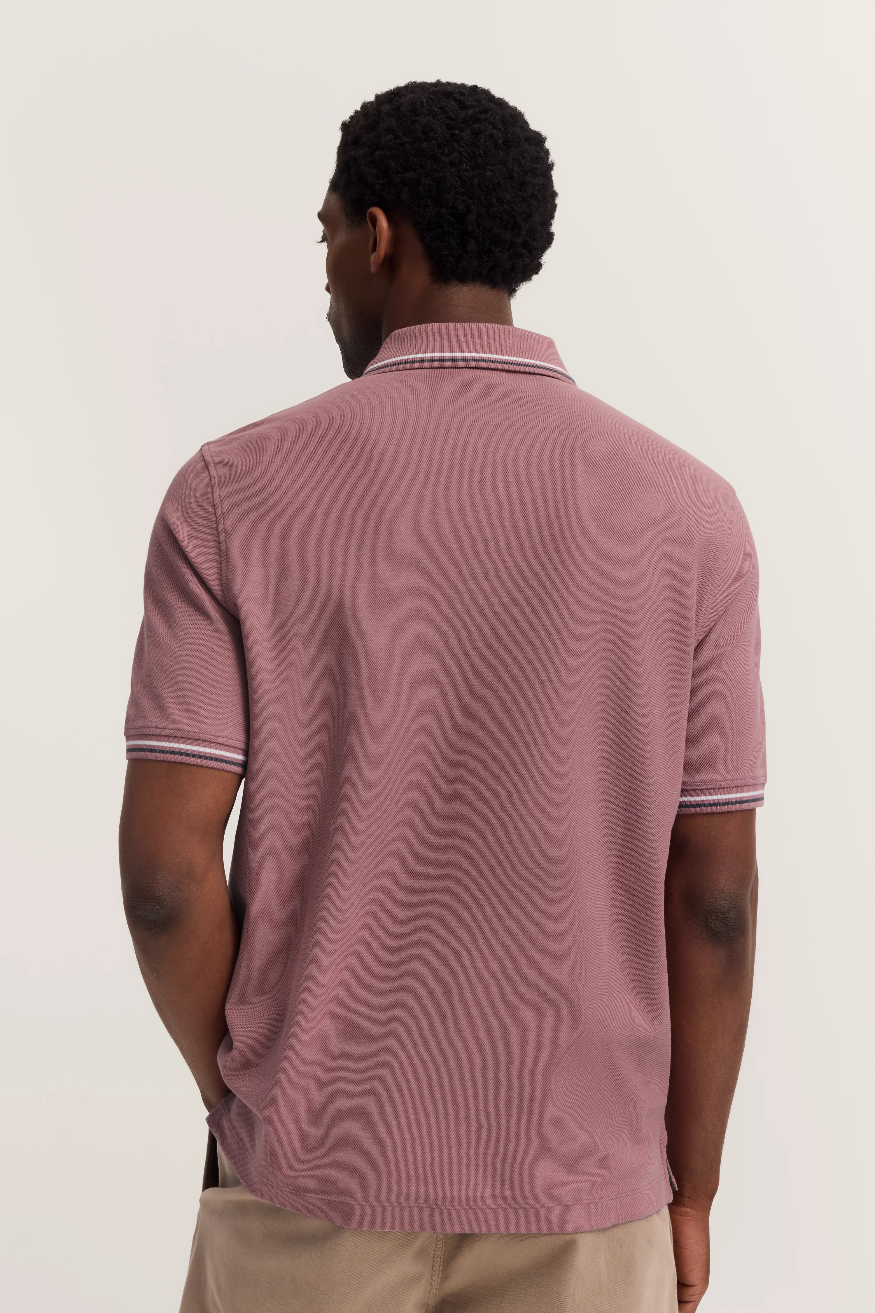 Achteraanzicht van model in roze bugatti poloshirt met beige kraag en details.