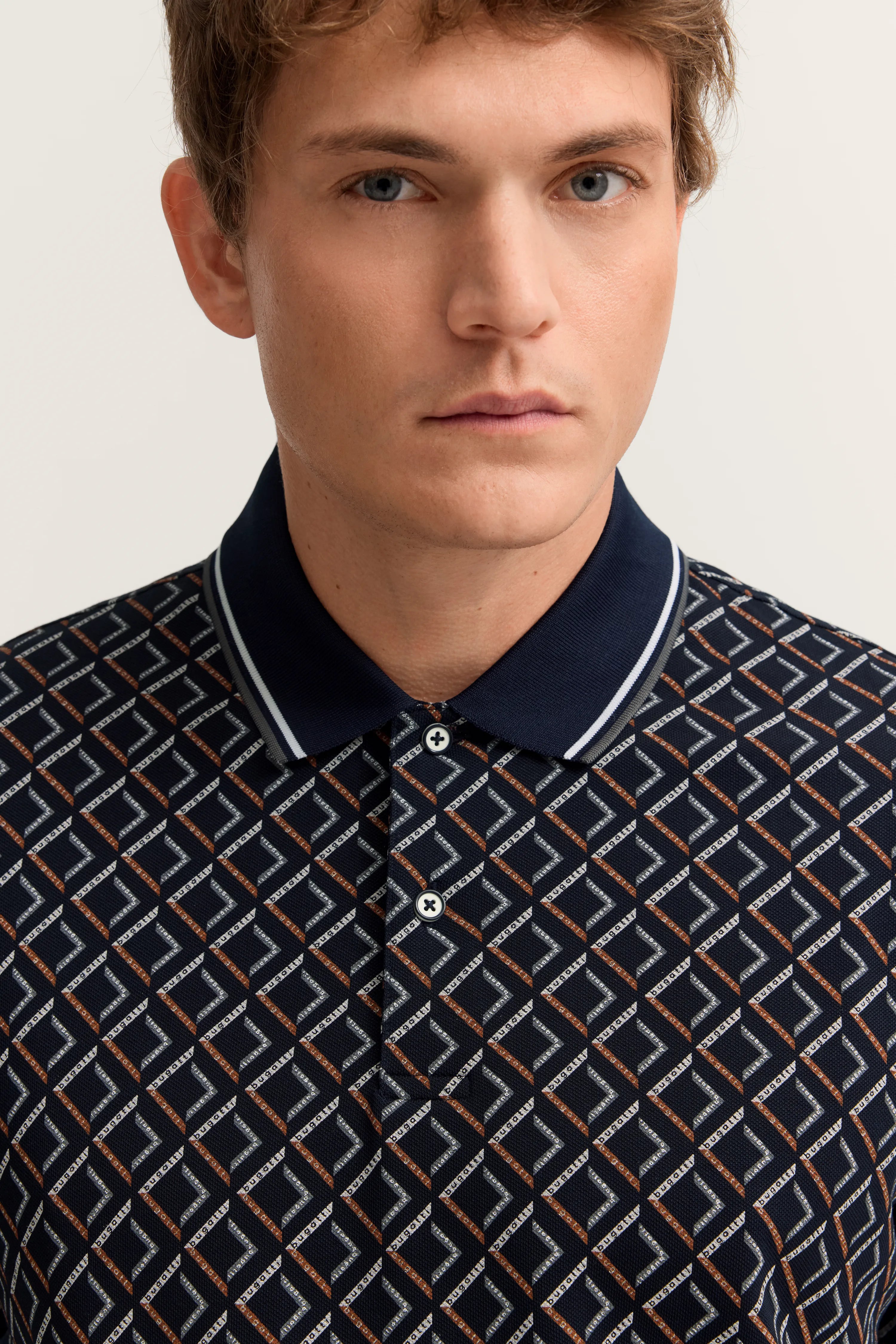 Büstenbild mit gemustertem Polo in Blau mit geometrischem Design, getragen von einem Modell.