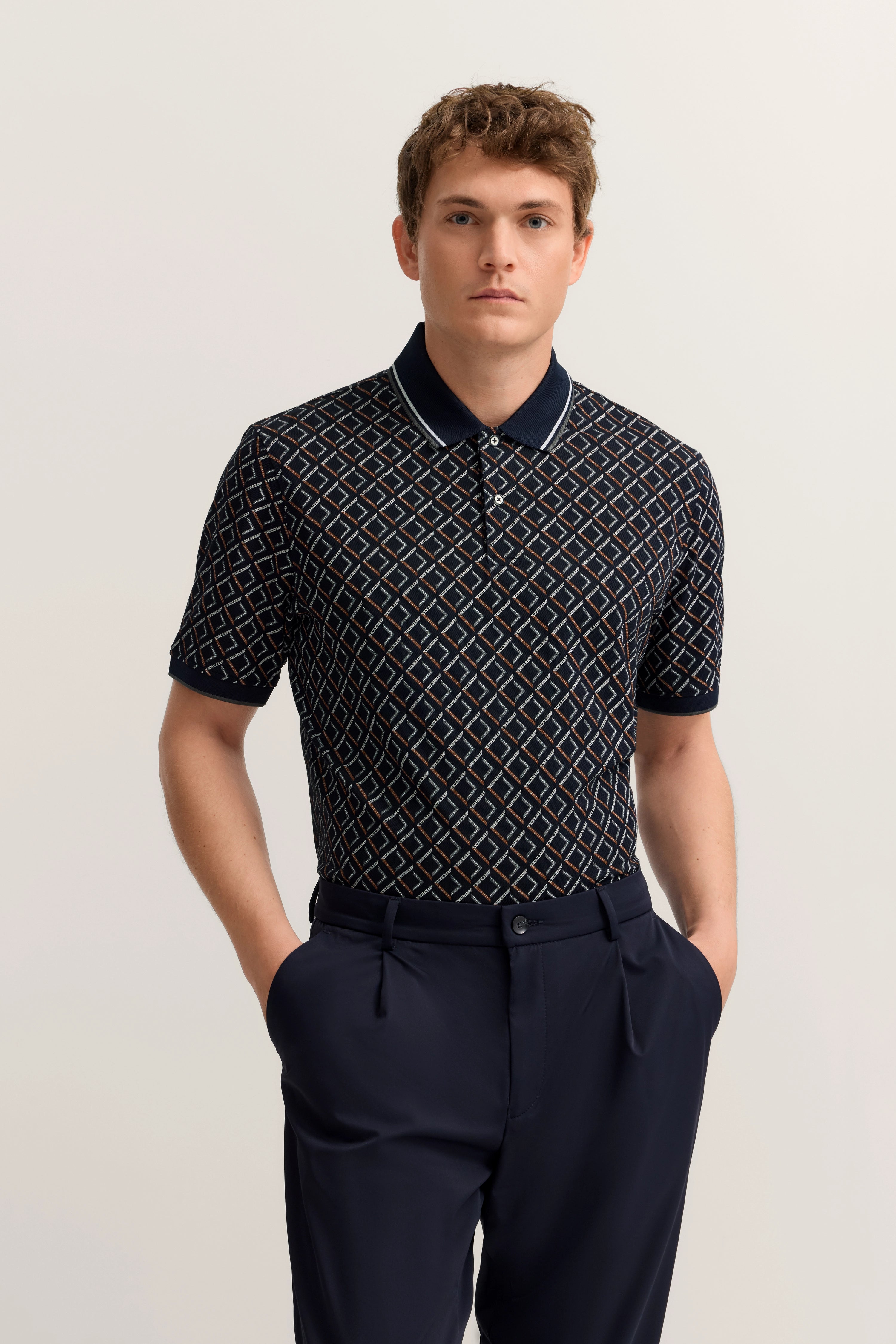 Model trägt bugatti Polo mit geometrischem Muster in Dunkelblau, lässig posierend mit Händen in Hosentaschen.