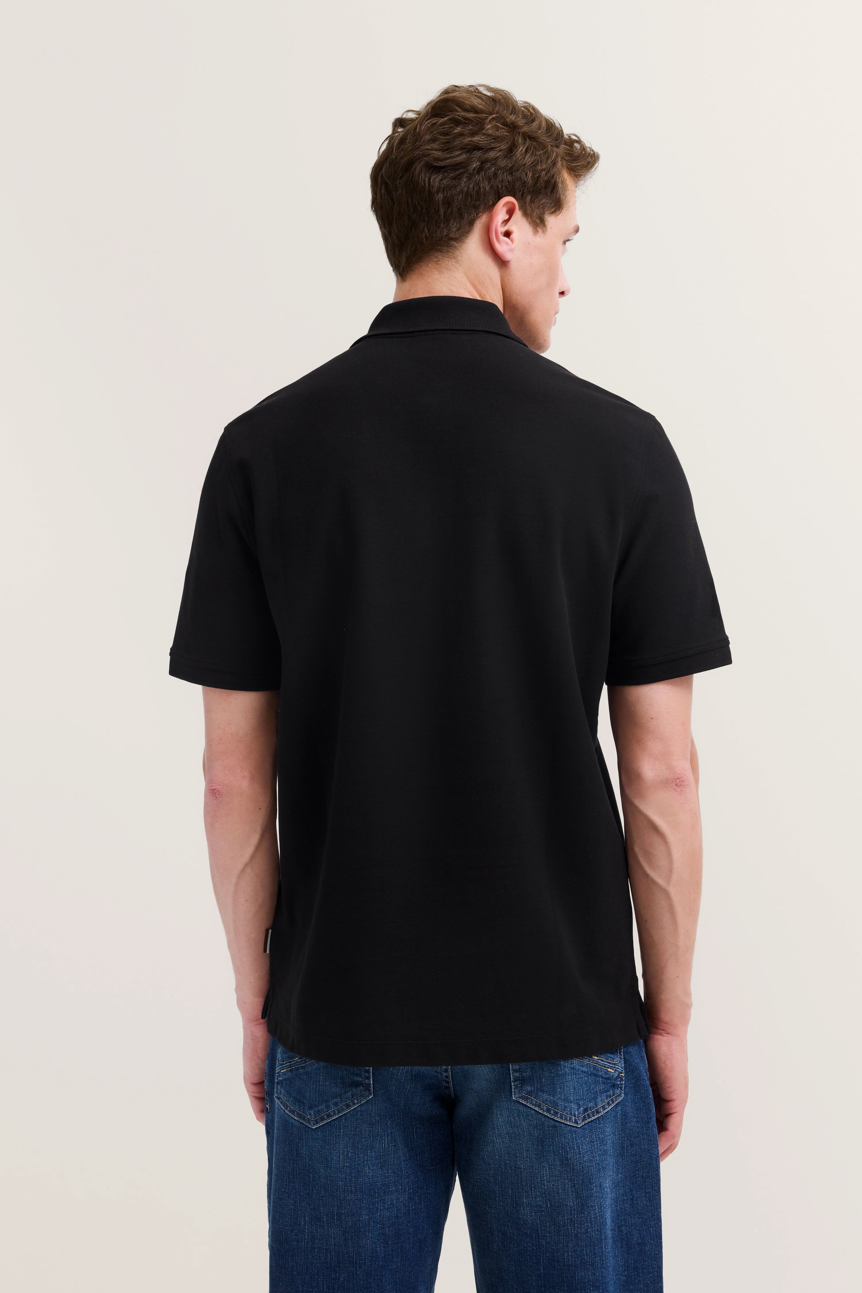 Schwarzes bugatti Poloshirt und blaue Jeans, Rückansicht Model, entspannte Haltung.