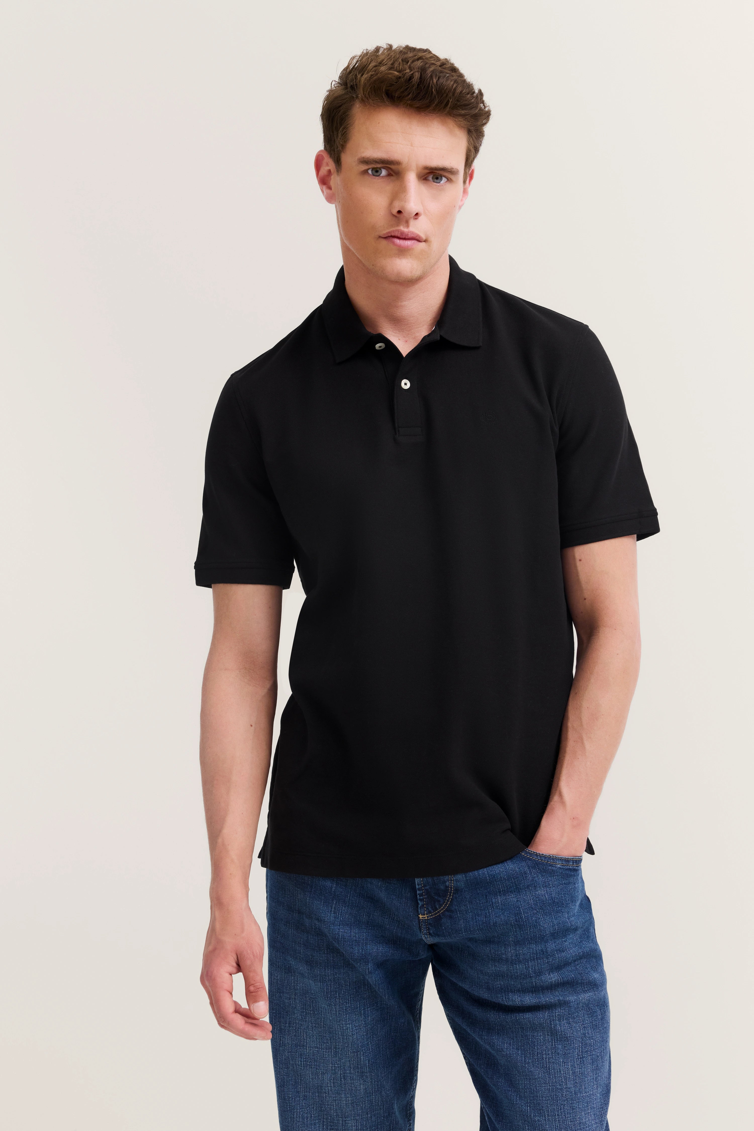 Schwarzes Polohemd, blaue Jeans, legeres Modelbild, entspannte Pose.