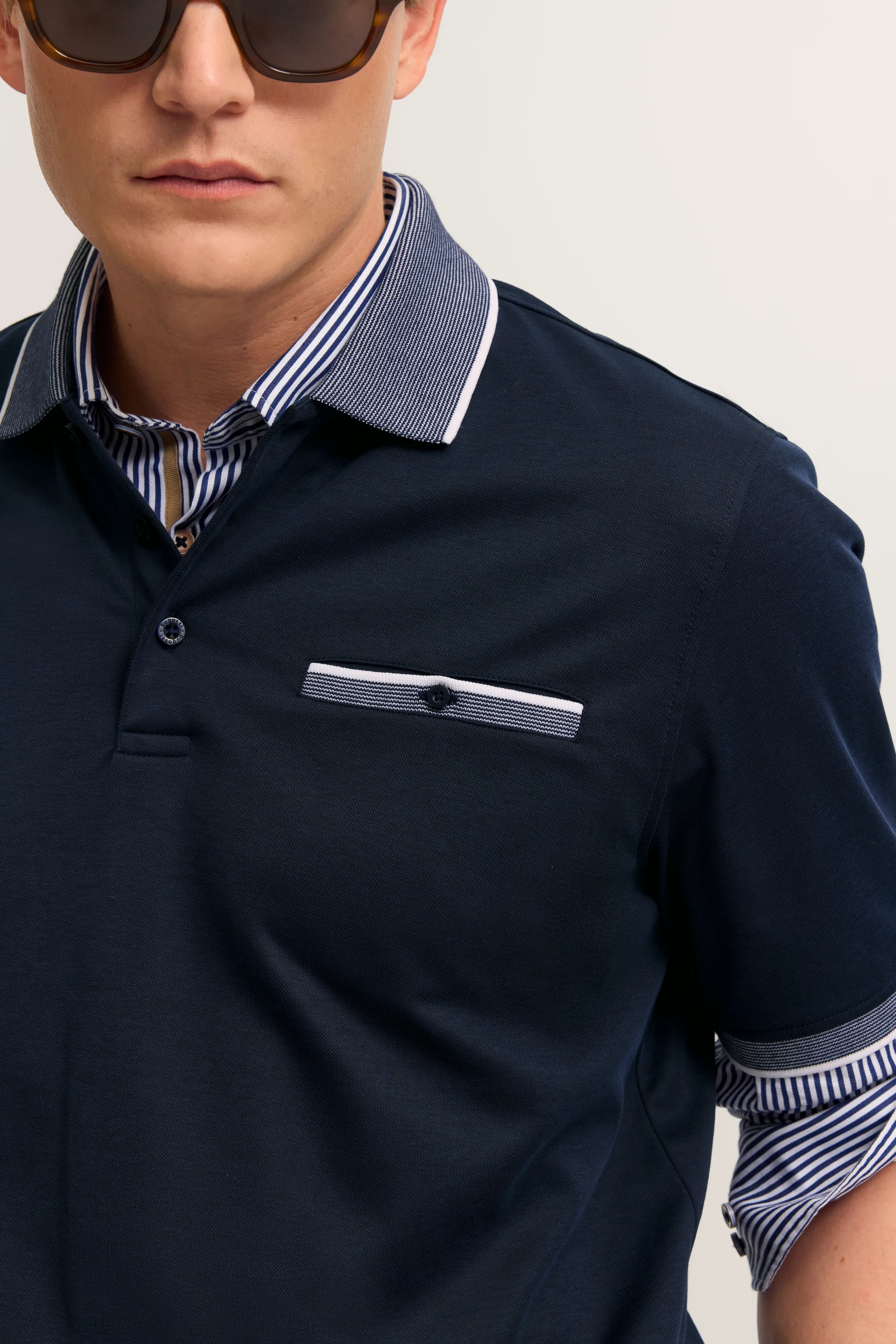 Dunkelblaues bugatti Poloshirt mit gestreiftem Kragen und Brusttasche, Modelbild mit lässiger Pose.