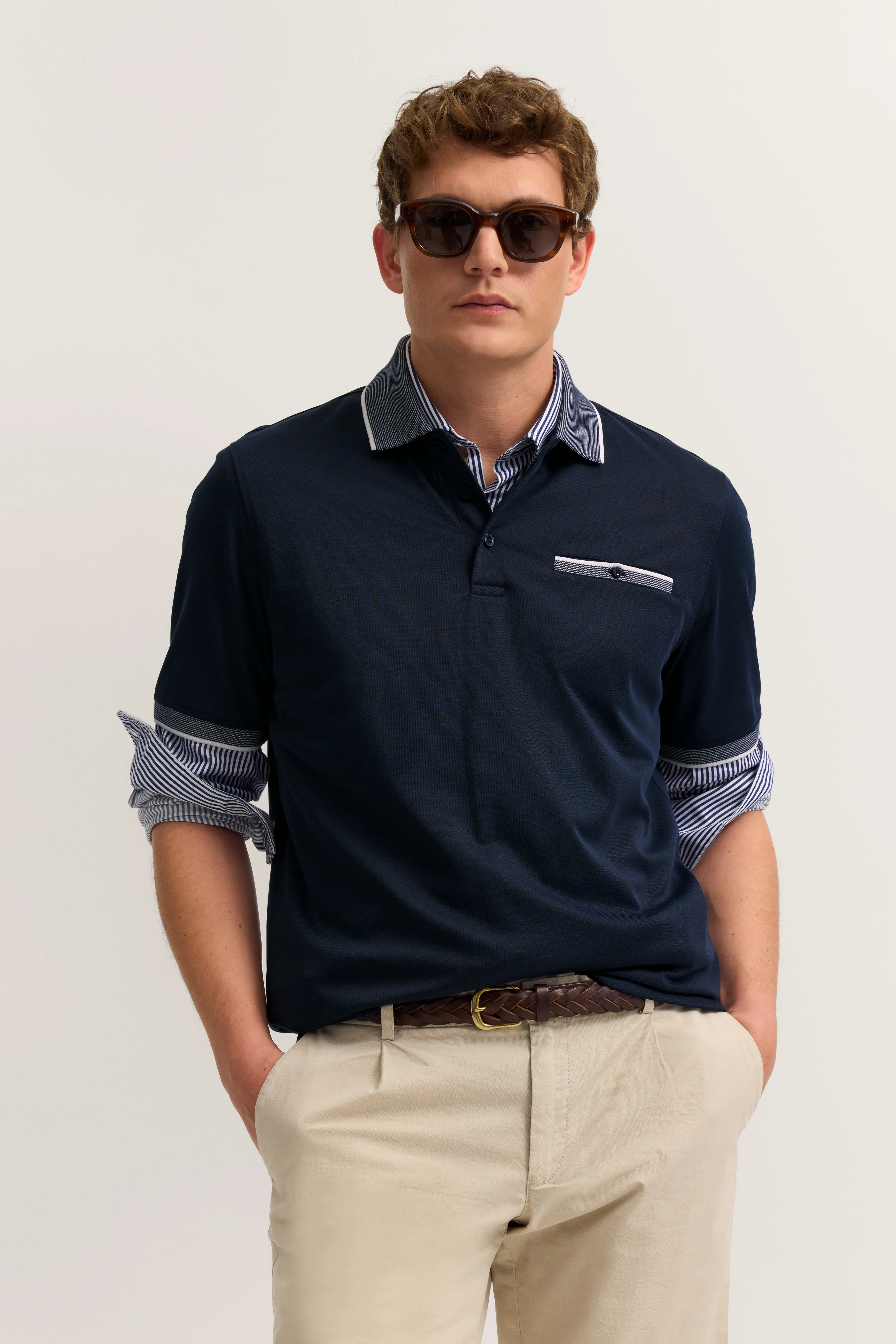 Navy Polo und gestreiftes Hemd, beige Chinos, Model mit Sonnenbrille, lässige Pose.