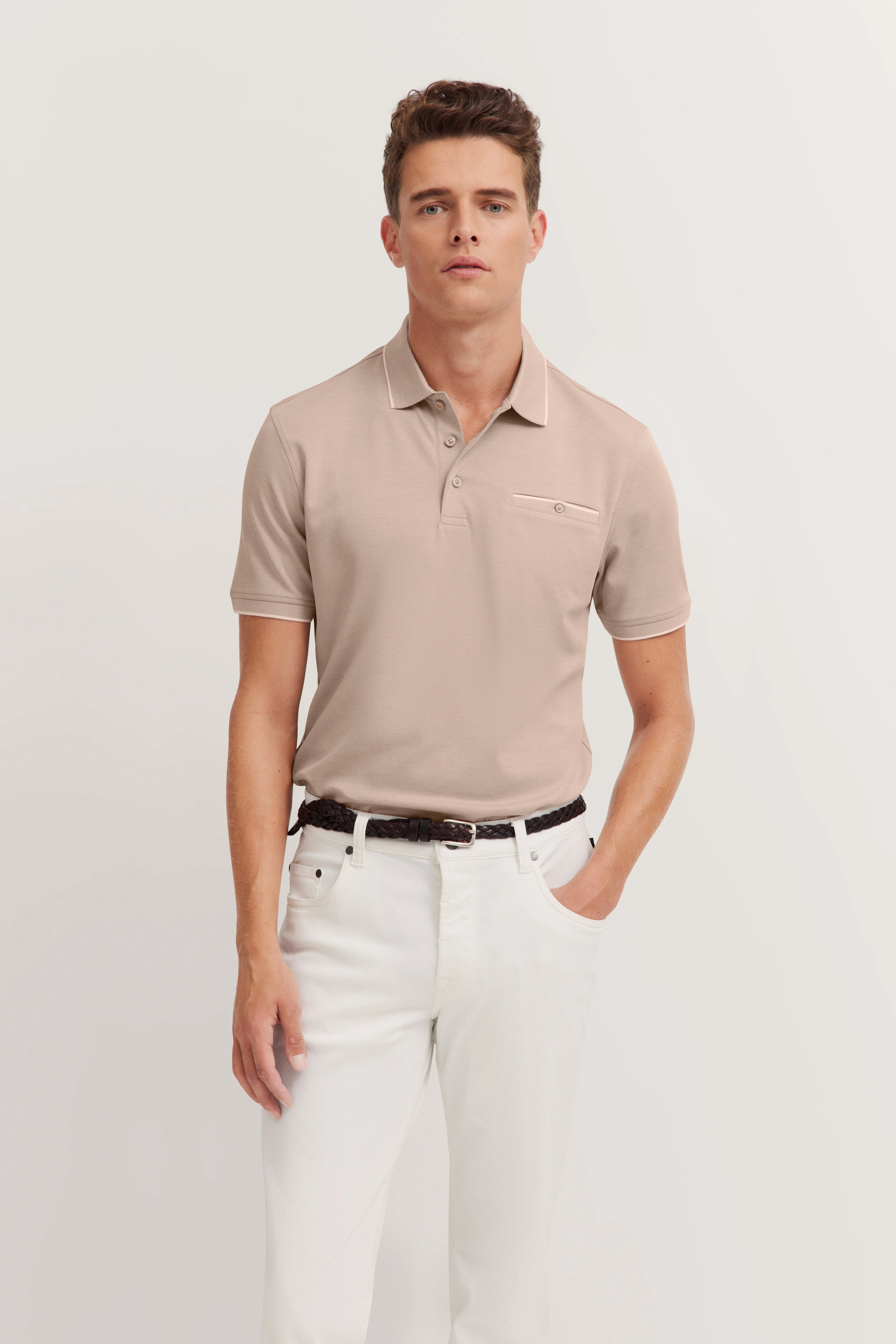 Beige polo shirt and white trousers, model standing with hands in pockets, exuding bugatti's refined style.