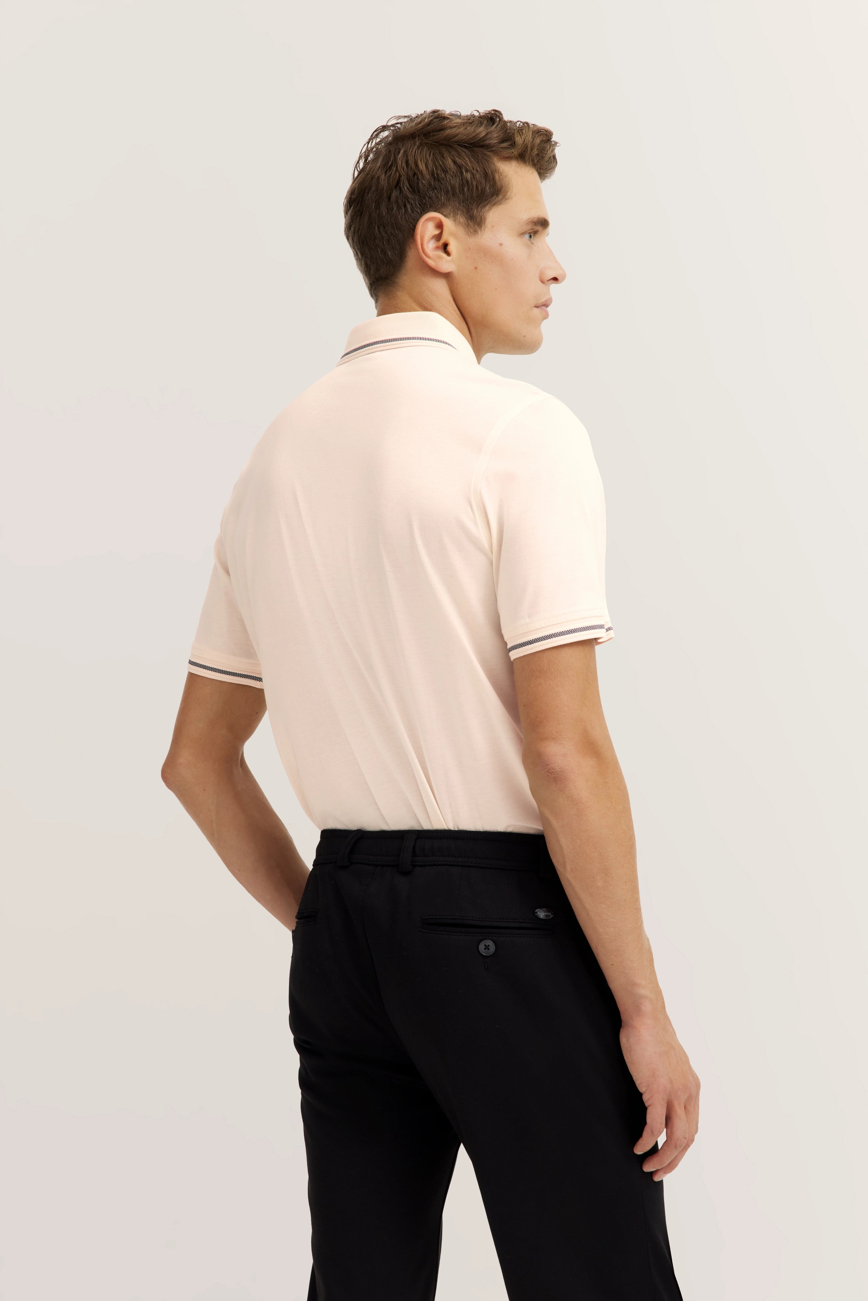 Model in cream polo and black pants, back view, relaxed pose.