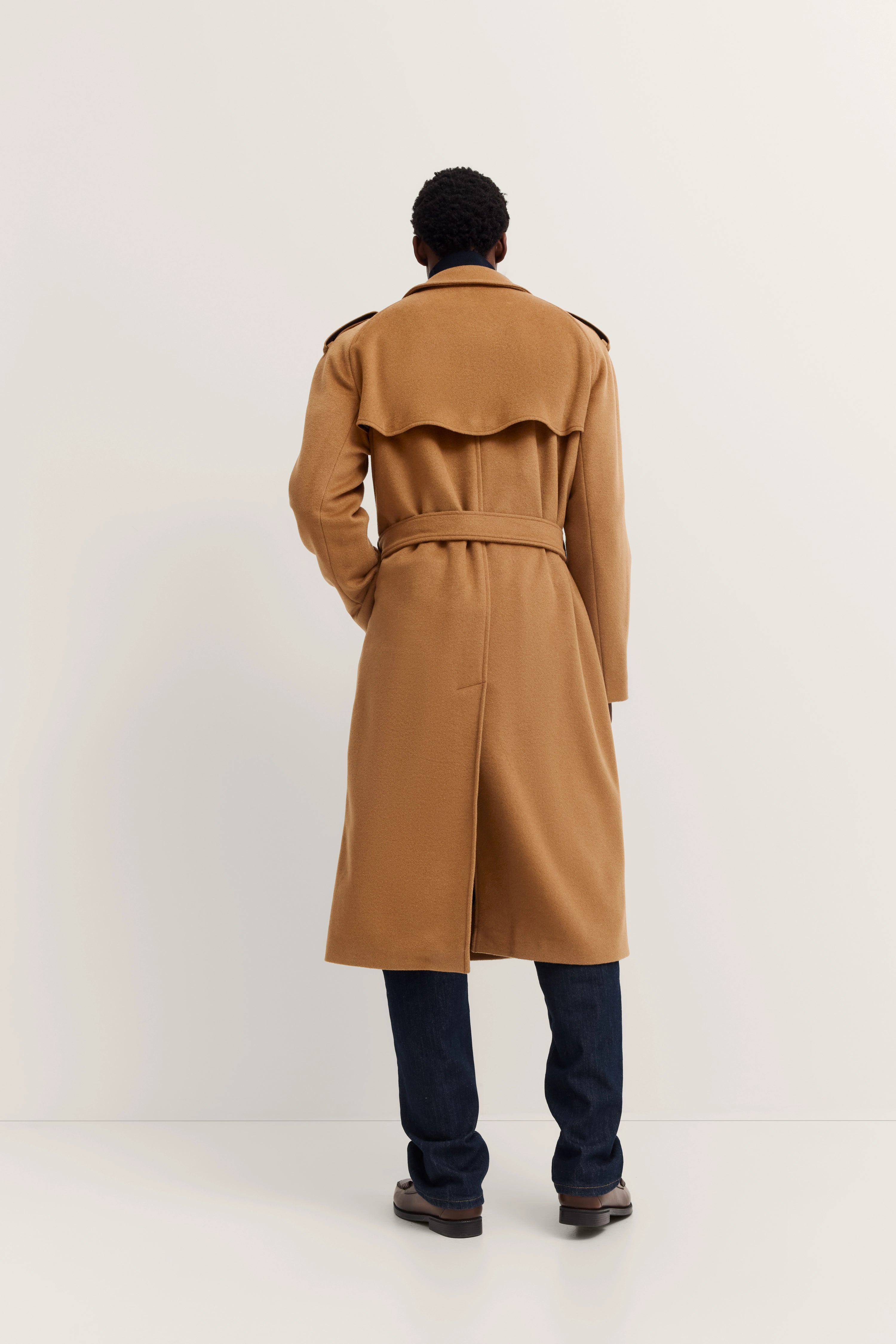bugatti model in long camel trench coat, dark jeans, relaxed pose from behind.