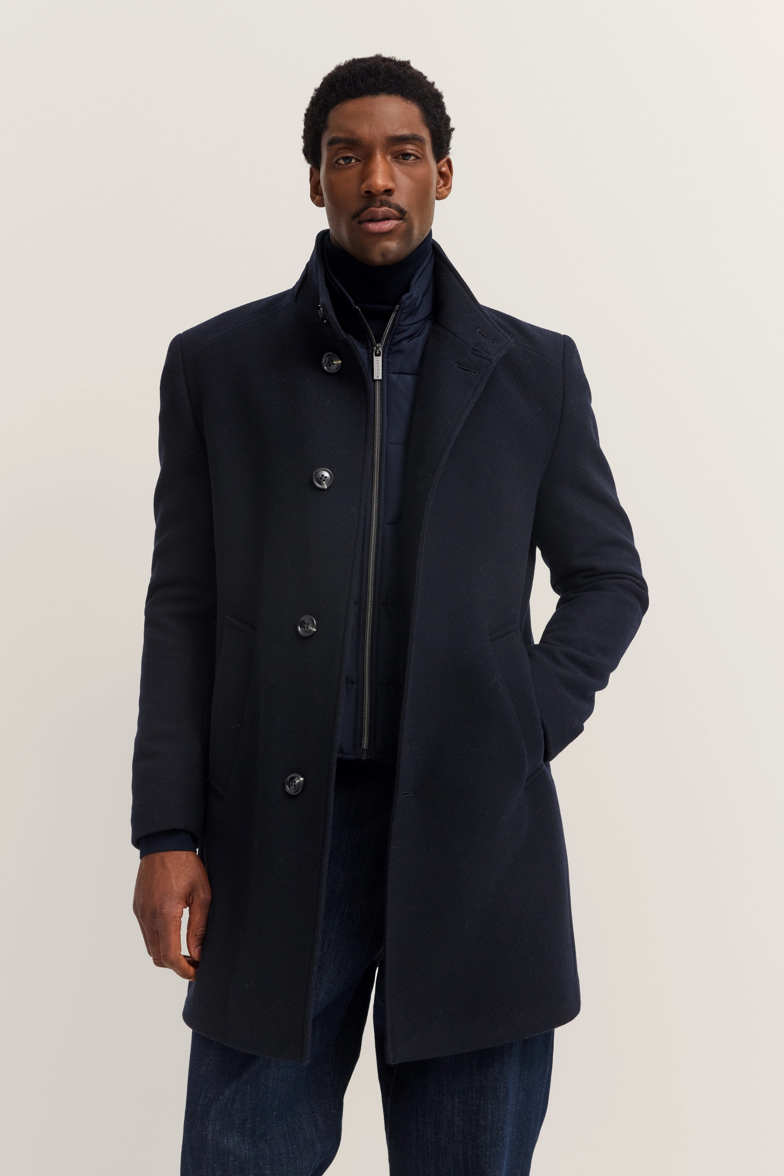Dark blue bugatti coat with stand-up collar, model pose, relaxed, stylish, and timeless.