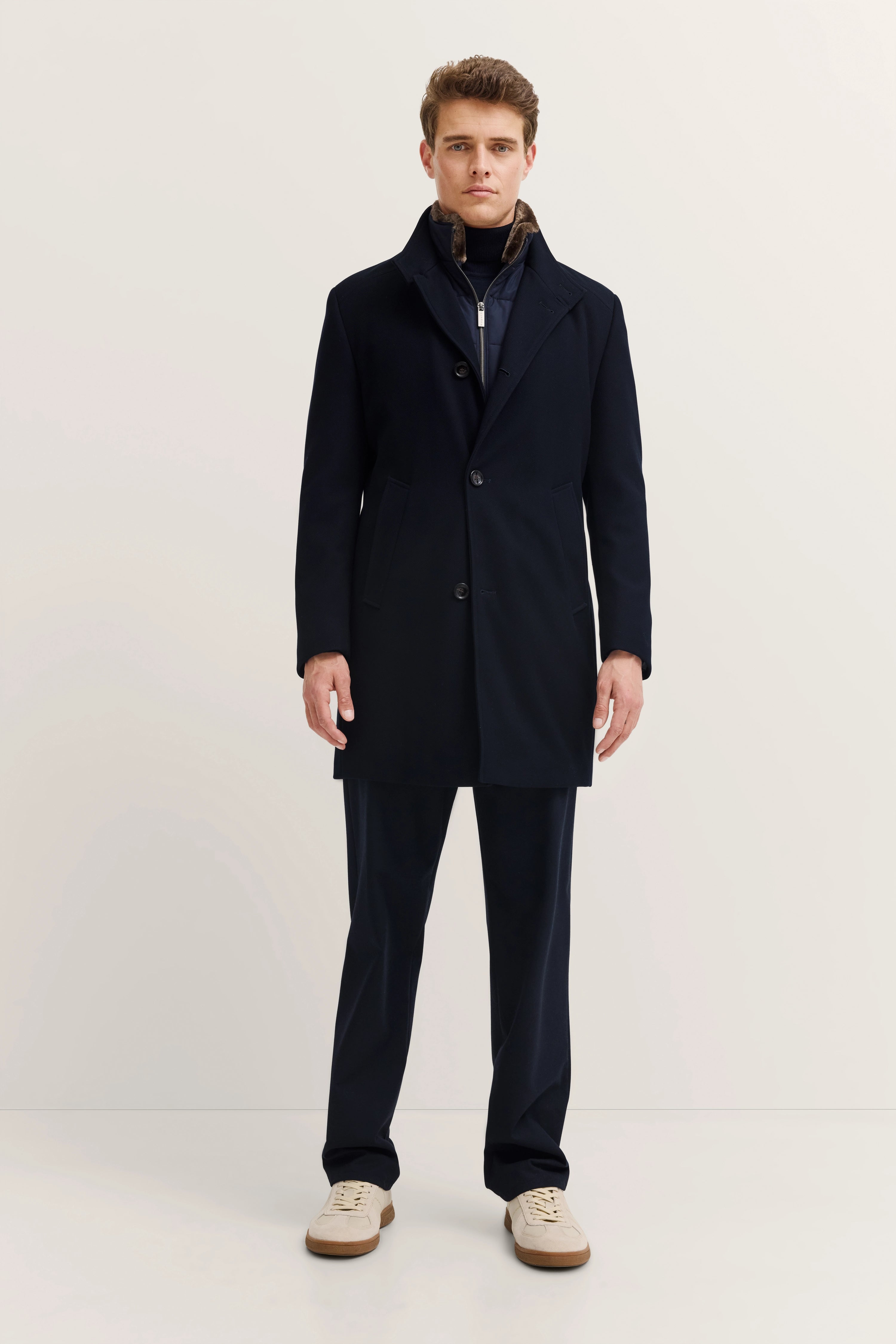 Model in elegantem, dunkelblauem bugatti Mantel und Hose, stehend, mit legerem Posing.